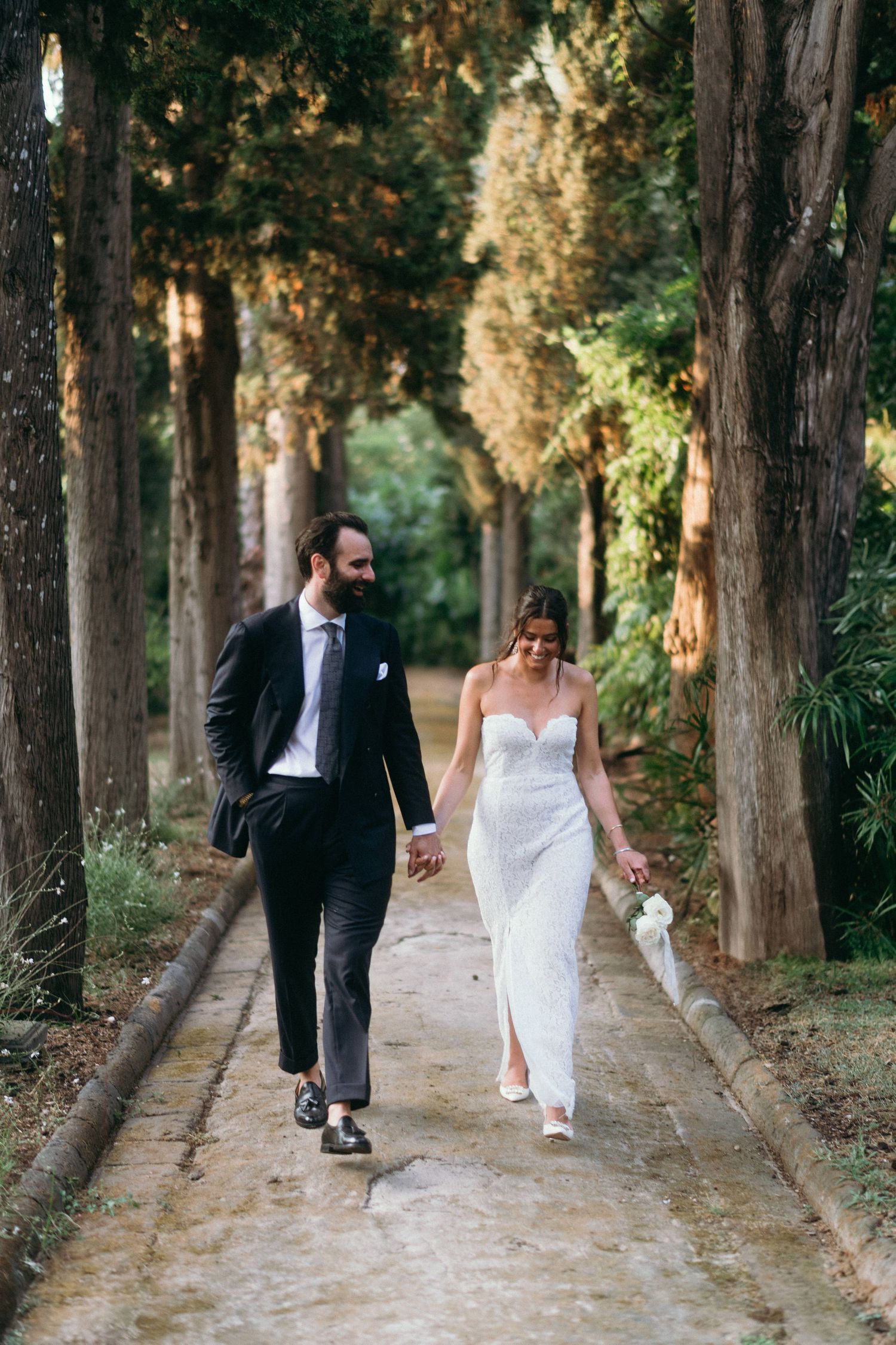A couple walks together on a tree-lined path in a romantic wedding photo sequence.