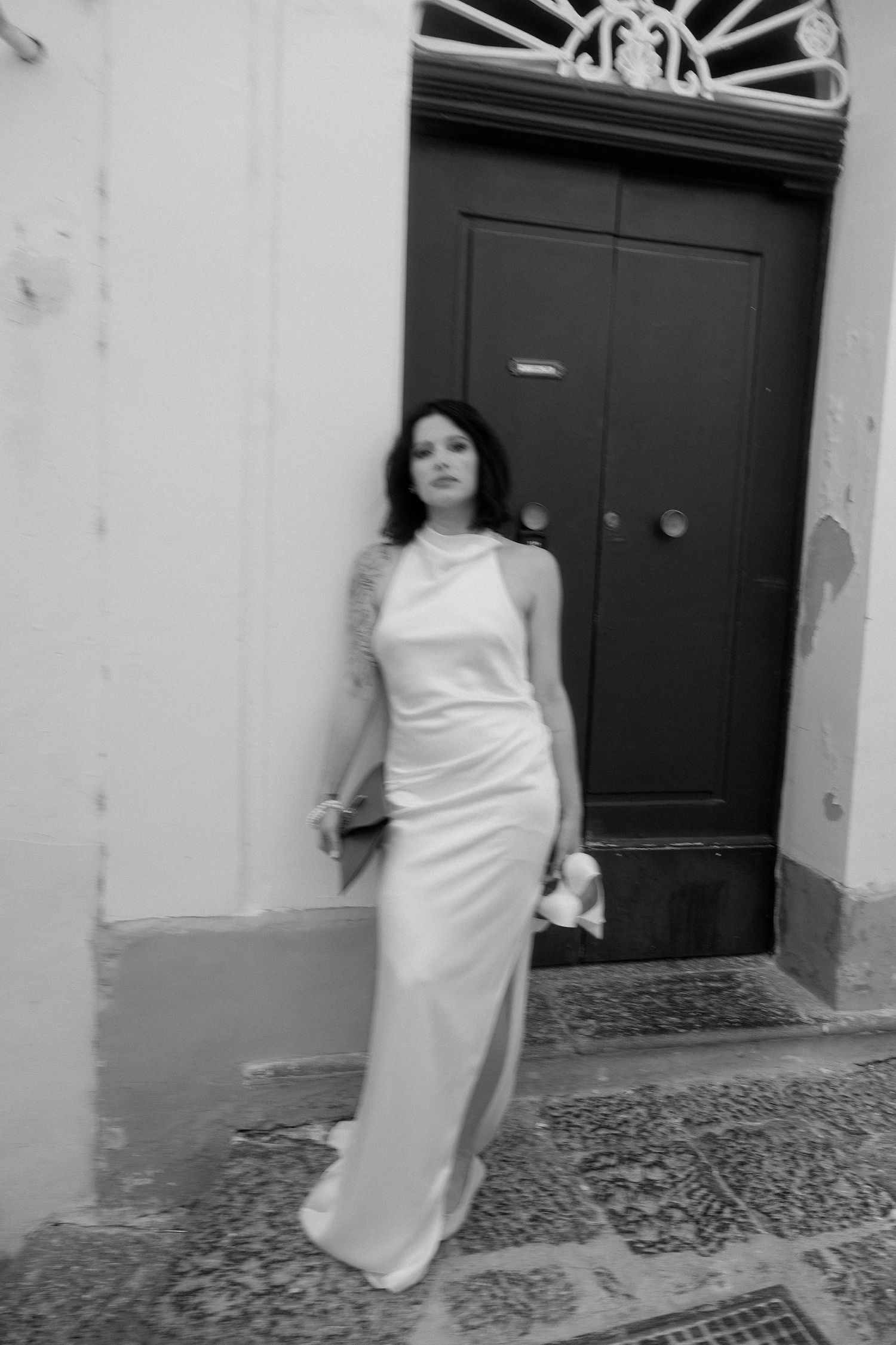 A sequence of black and white photos shows a person in a white dress walking along a cobblestone street near doorways.
