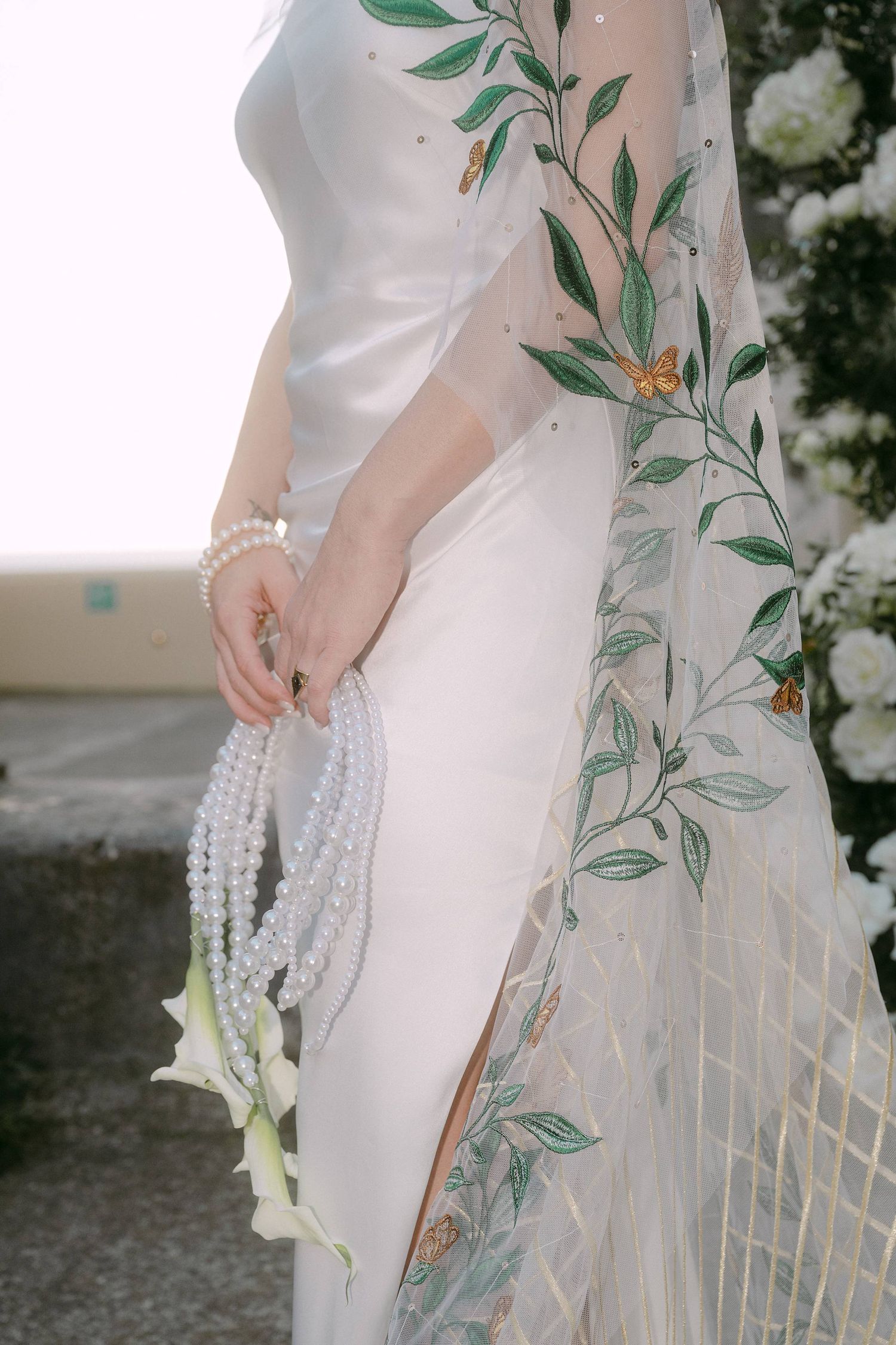 Elegant white wedding dress with delicate green leaf embroidery detail and pearl accessories.