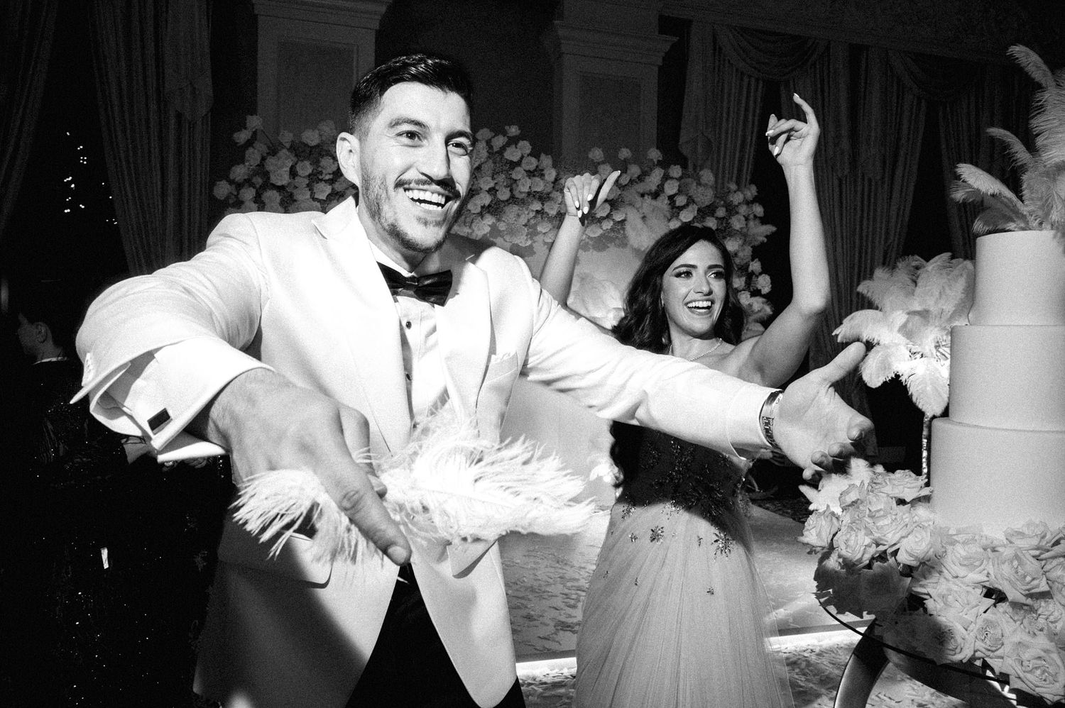 Black and white photo of joyful newlyweds celebrating at their wedding reception with dancing and laughter.