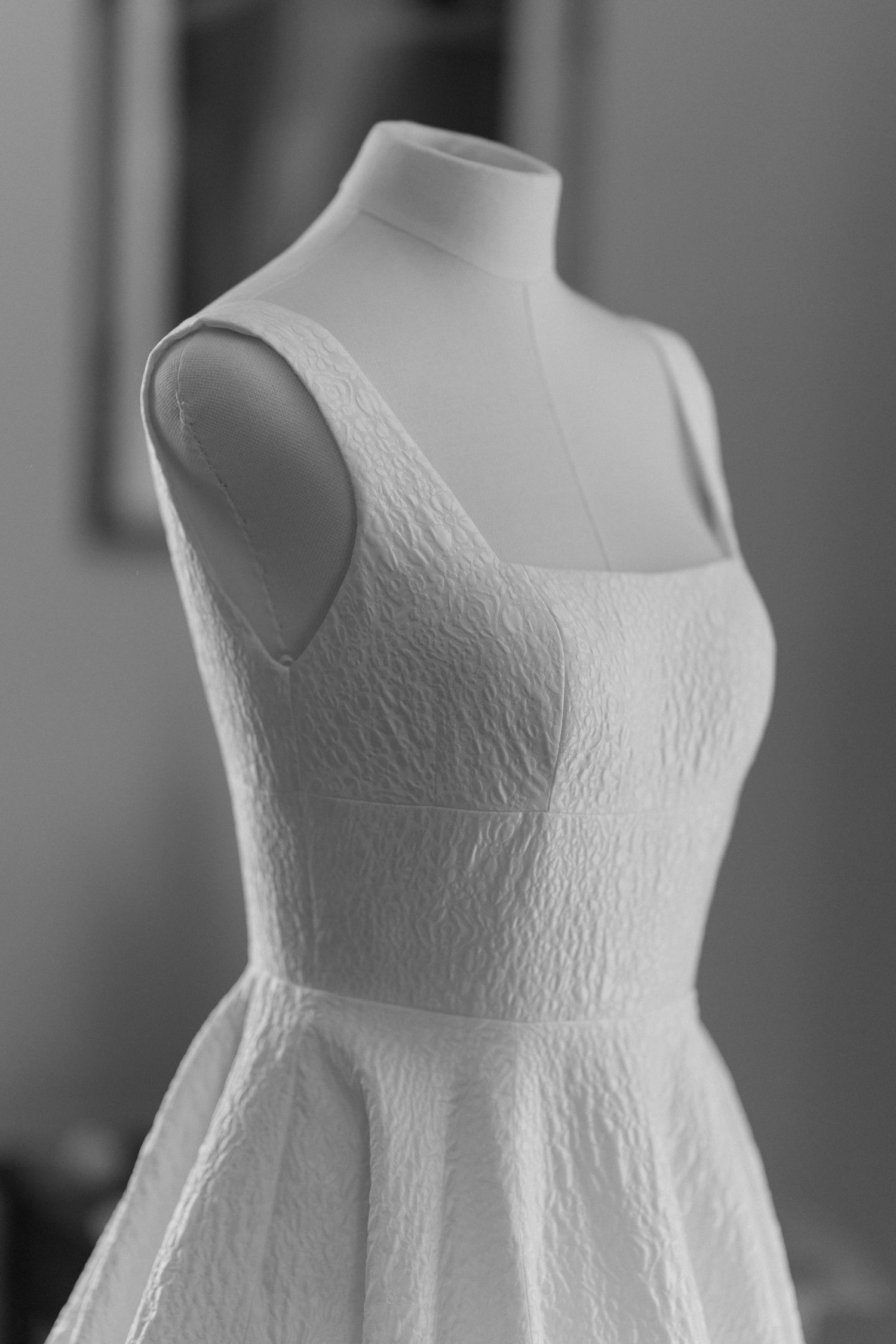 Close-up view of a white wedding dress bodice on a mannequin showing delicate embroidered lace pattern details.