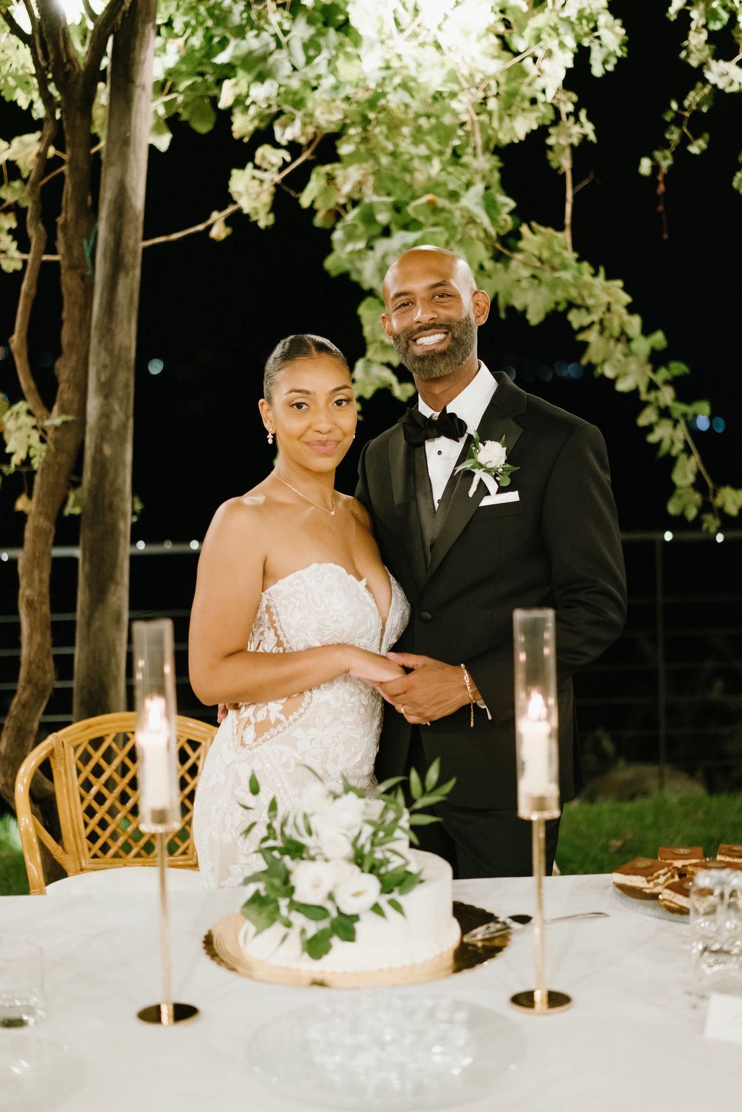 A happy couple shares joyful moments during their wedding reception while sitting at an elegant table with white decor.