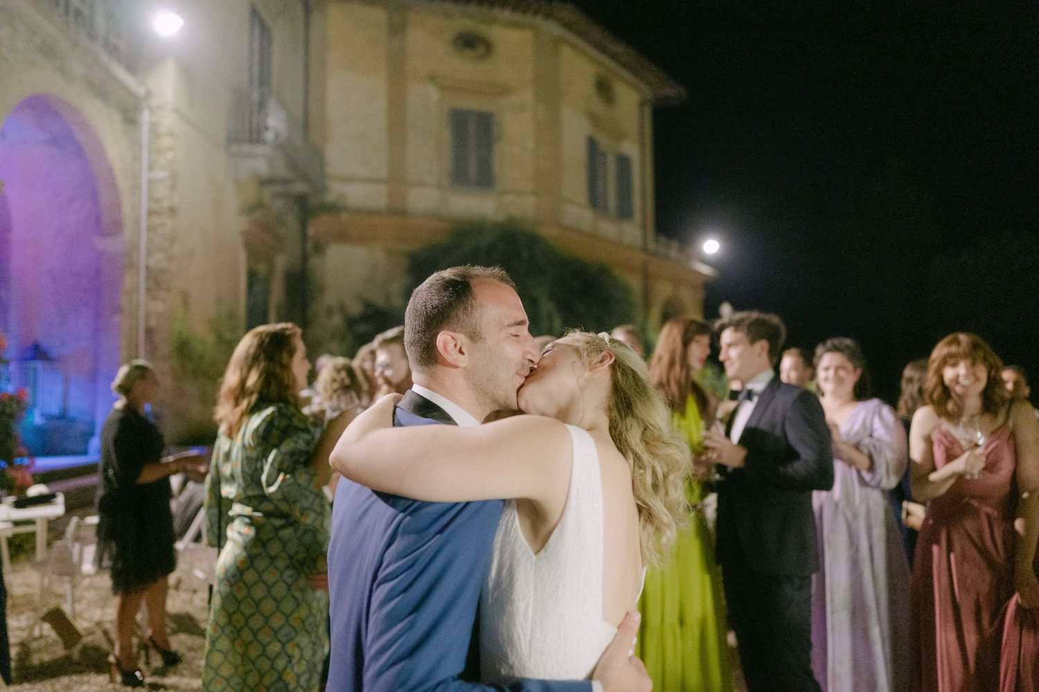 Couples dance together at an elegant evening wedding reception with historic building and purple lighting in background.