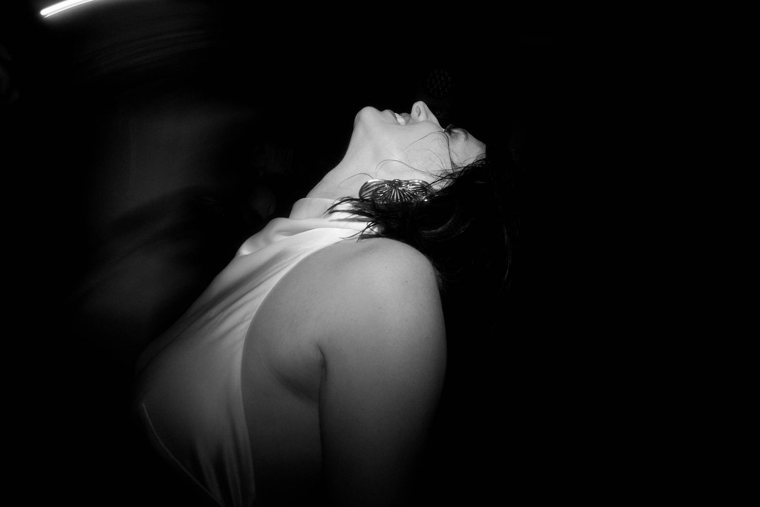 Dramatic black and white portrait showing a person's neck and shoulder in soft lighting against a dark background.