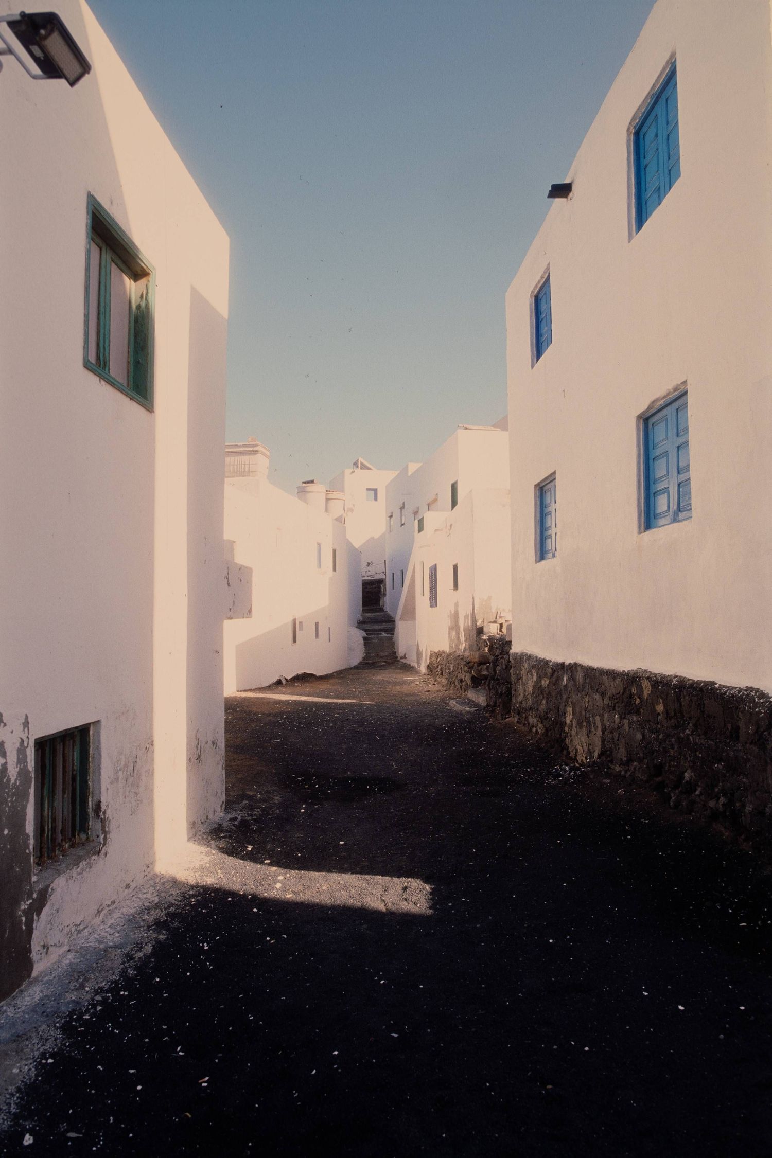 Narrow alley with white buildings and blue windows in a Mediterranean village showcases traditional architecture.