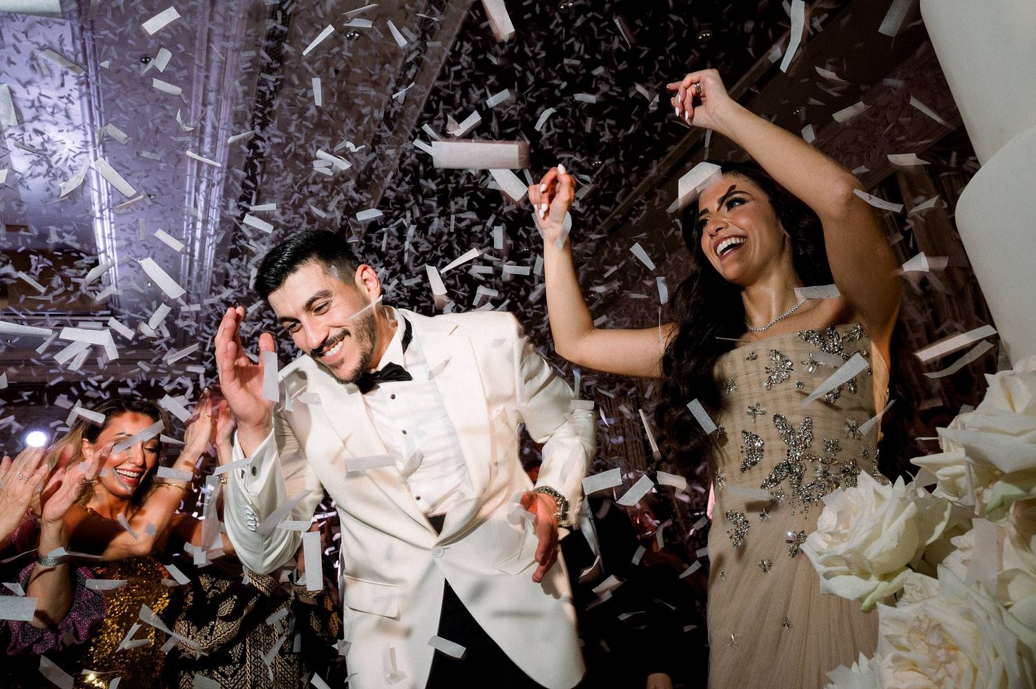 Happy couple dancing and celebrating under falling confetti at an elegant wedding reception party.