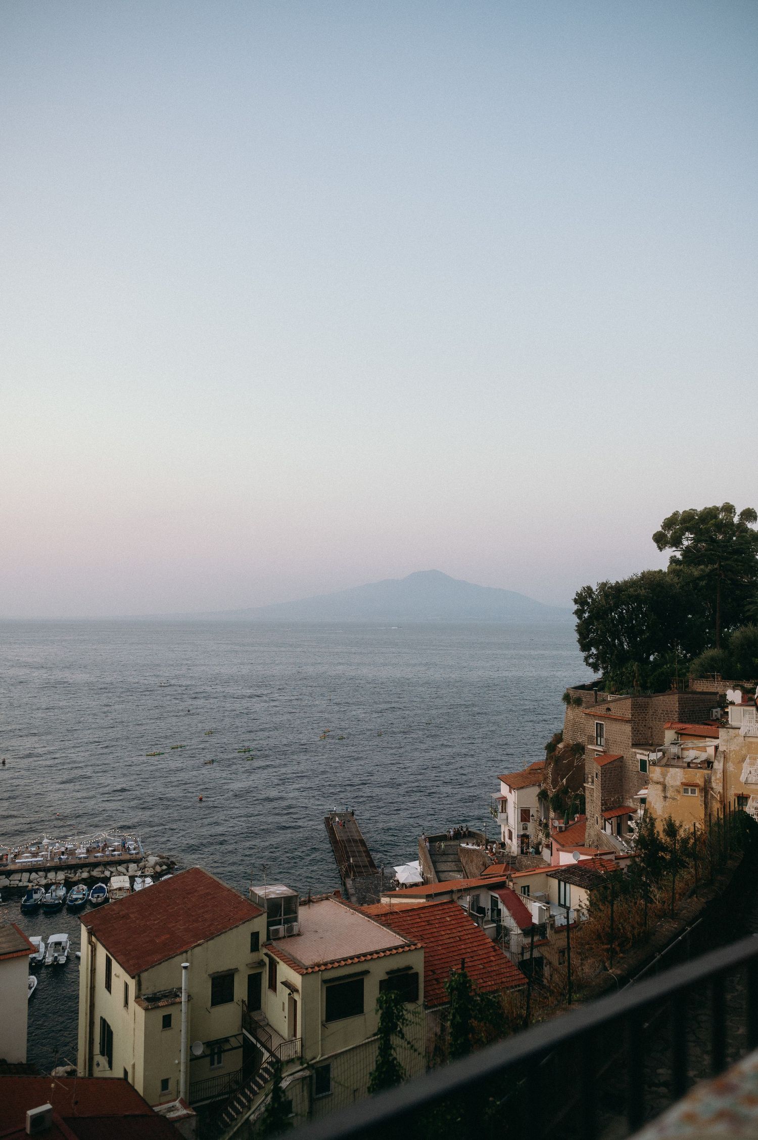 Coastal houses overlook the Mediterranean Sea with Mount Vesuvius visible in the distance during sunset in Sorrento, Italy.