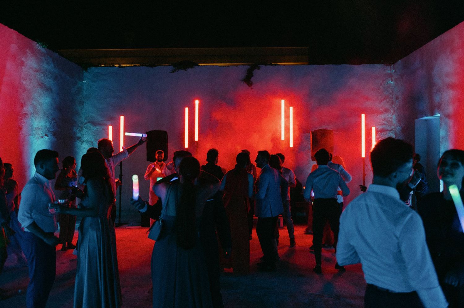 Crowd of people dancing at a nightclub with dramatic red and blue lighting effects illuminating the dark space.