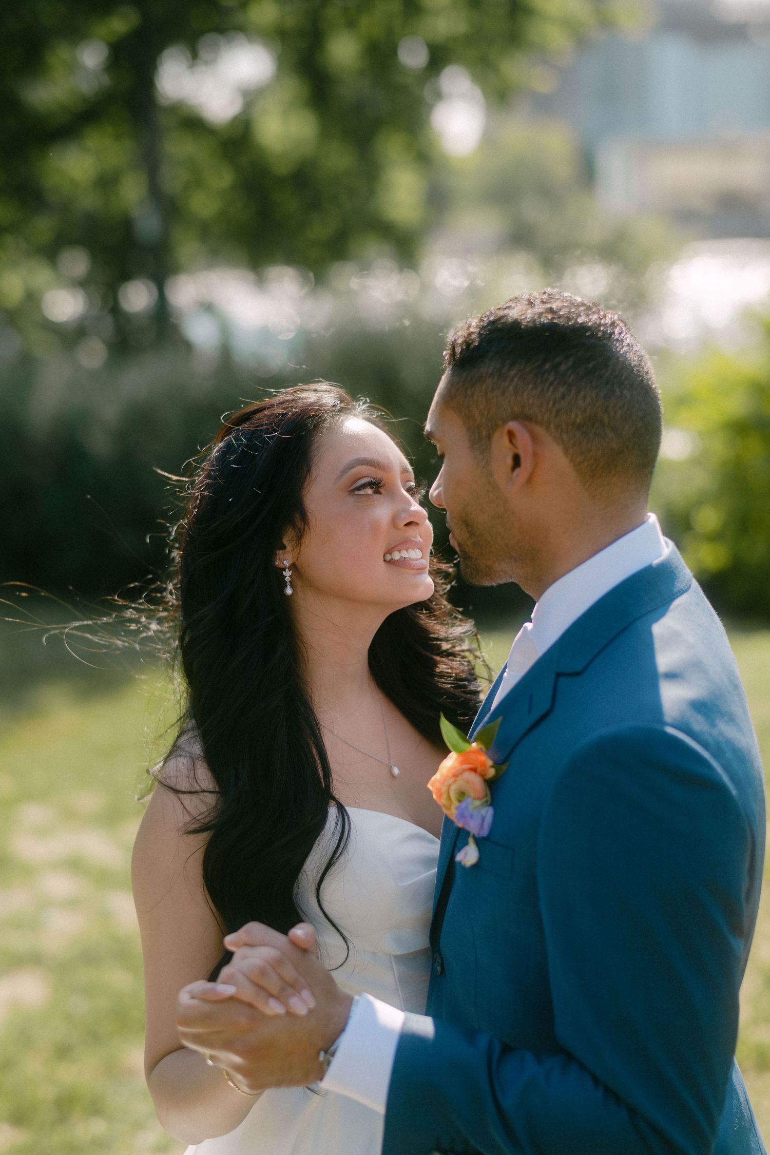 A happy couple shares intimate moments in a sunny outdoor setting wearing wedding attire and embracing tenderly.