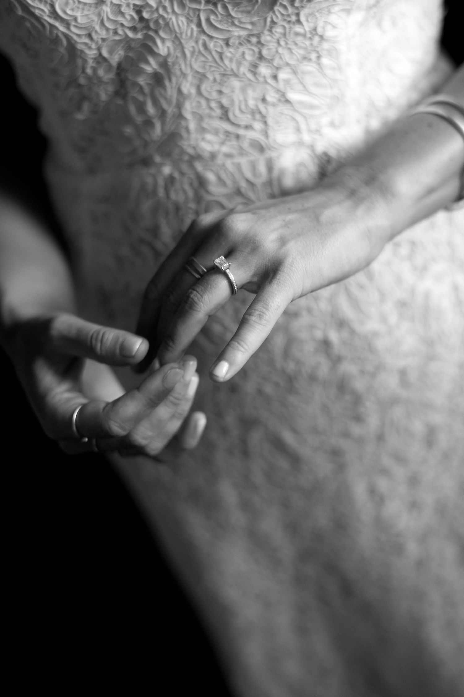 A black and white closeup of hands with wedding rings, showcasing matrimonial jewelry against white fabric.