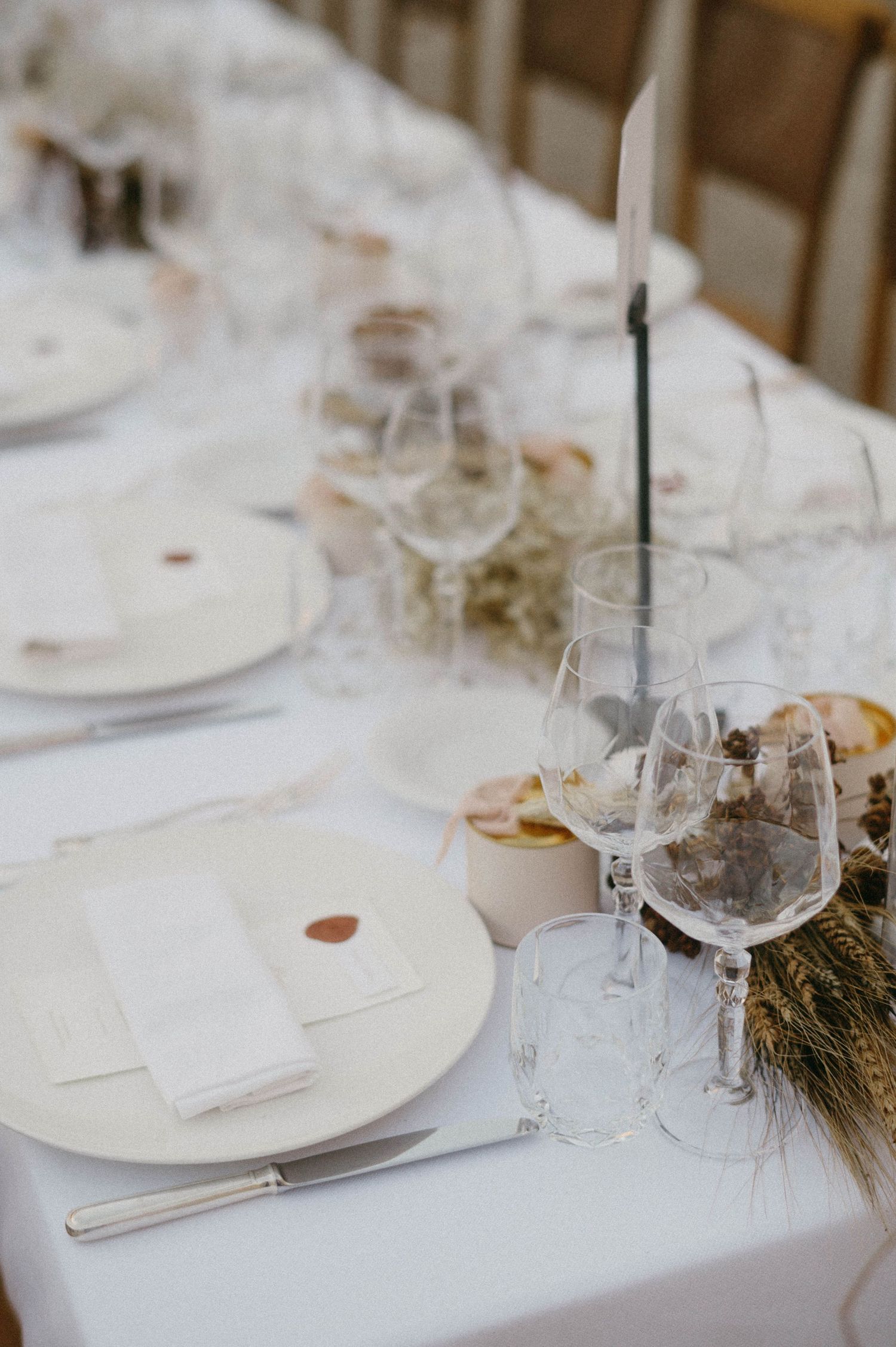 Elegant table setting with white plates, wine glasses and delicate decor on a crisp white tablecloth.