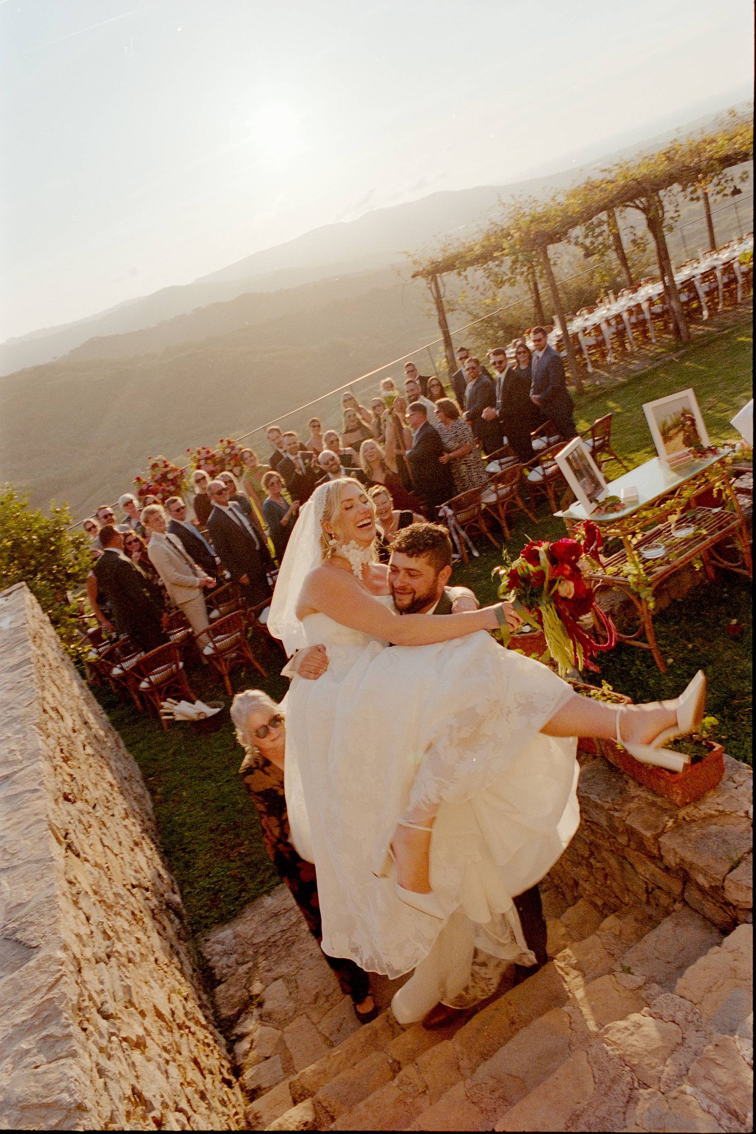 Wedding couple dips and spins on stone patio during sunset celebration with guests watching in background.