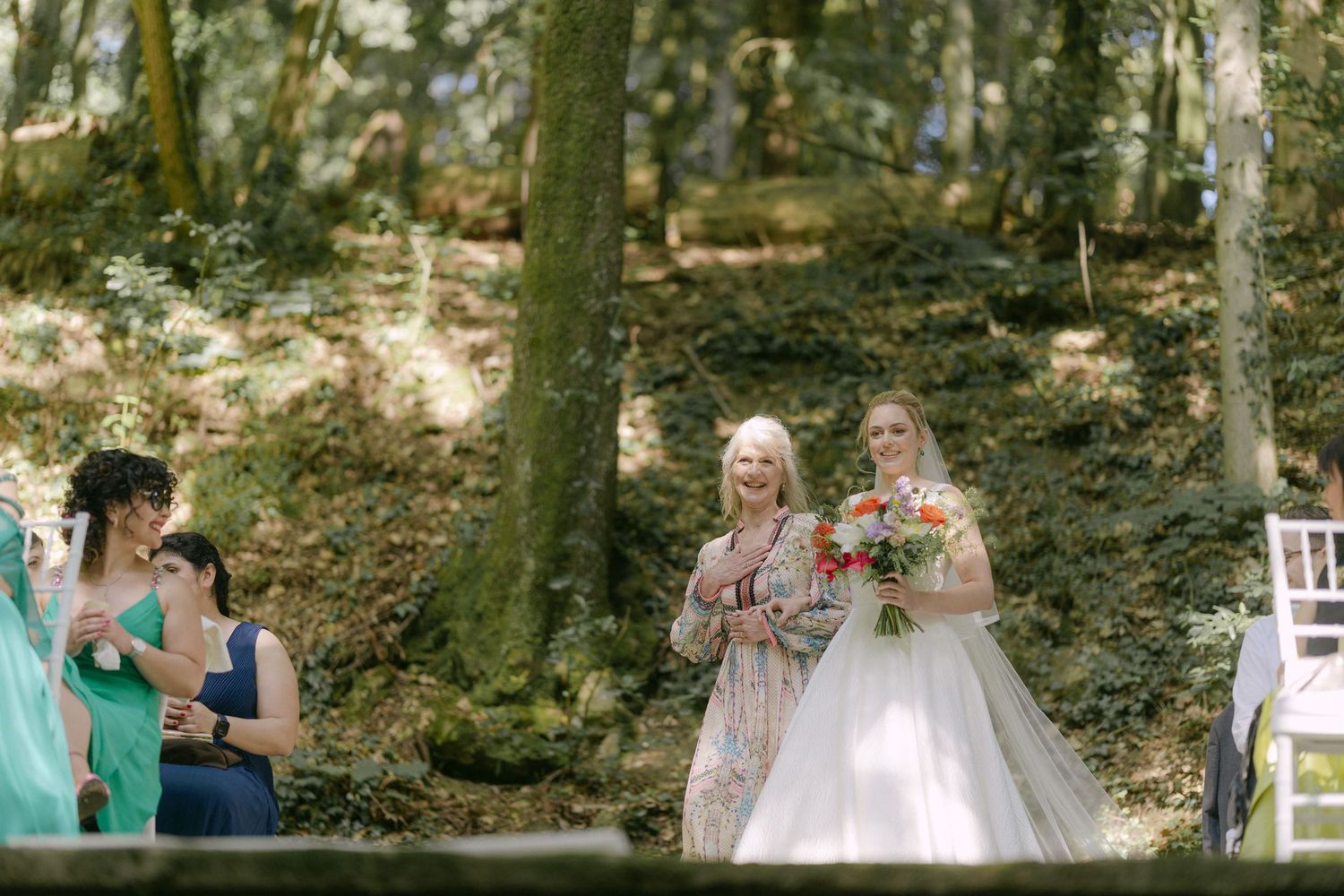 Wedding party members gather in a lush forest setting during an outdoor ceremony celebration.
