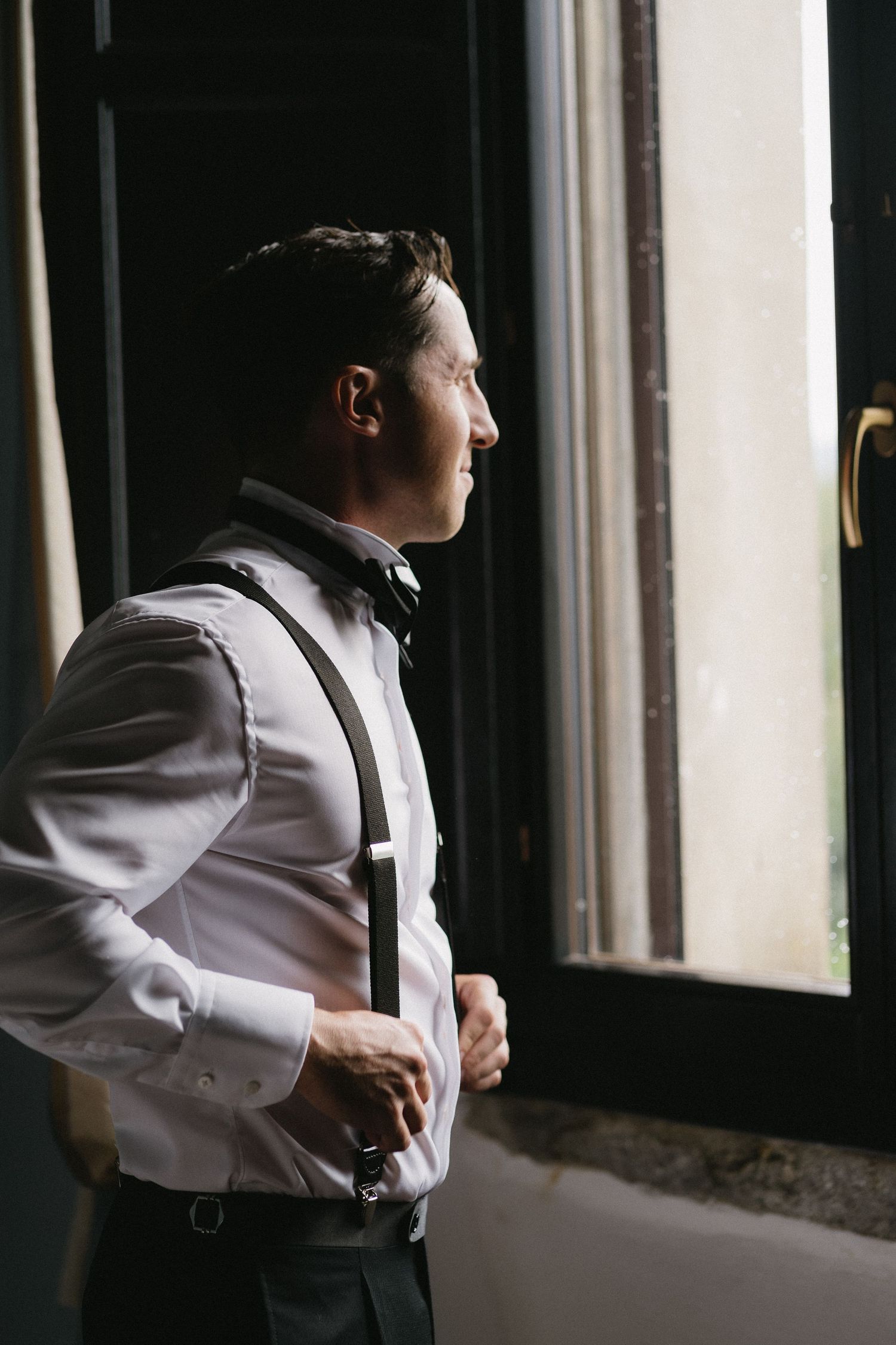 A person in a white dress shirt stands by a window in a dimly lit room creating multiple silhouette reflections.