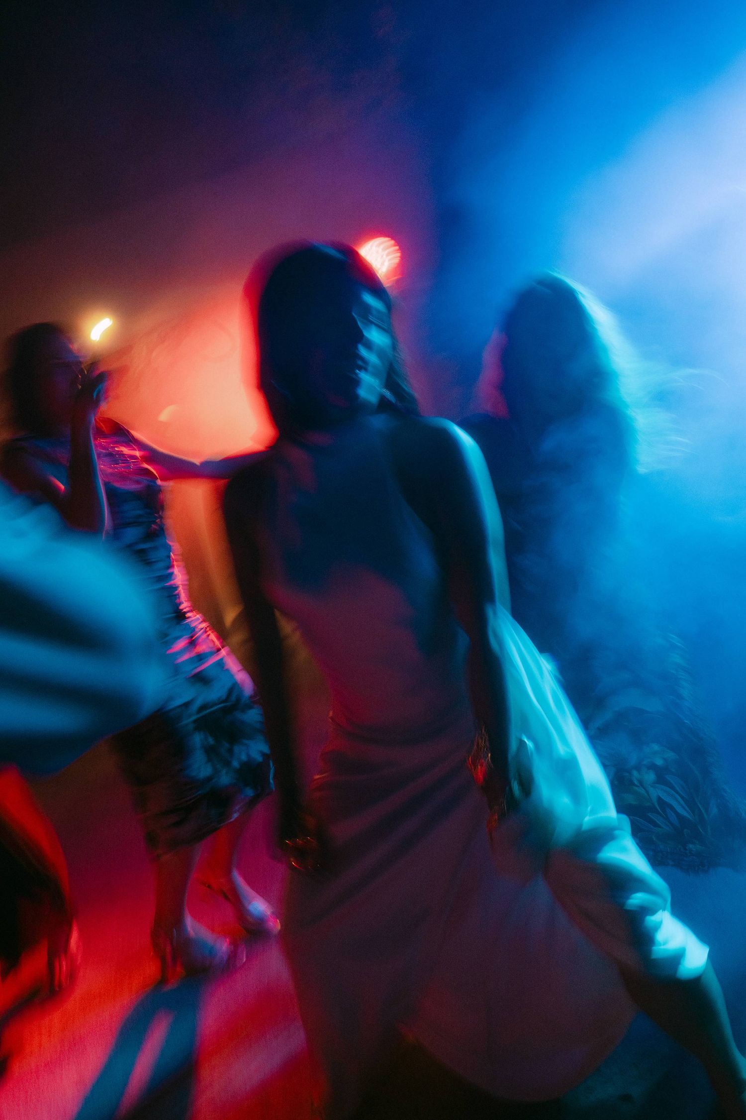 Silhouettes of people dancing in a nightclub with dramatic red and blue lighting effects creating a moody atmosphere.