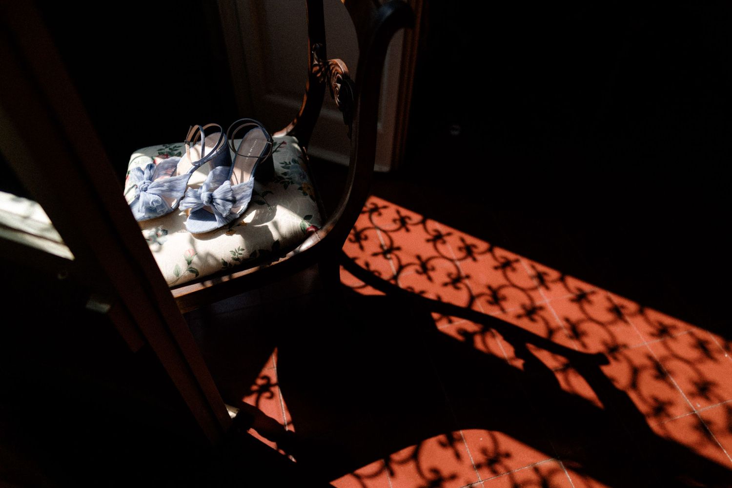 Dramatic shadows cast geometric patterns across a dark floor as sunlight streams through a window with decorative elements.