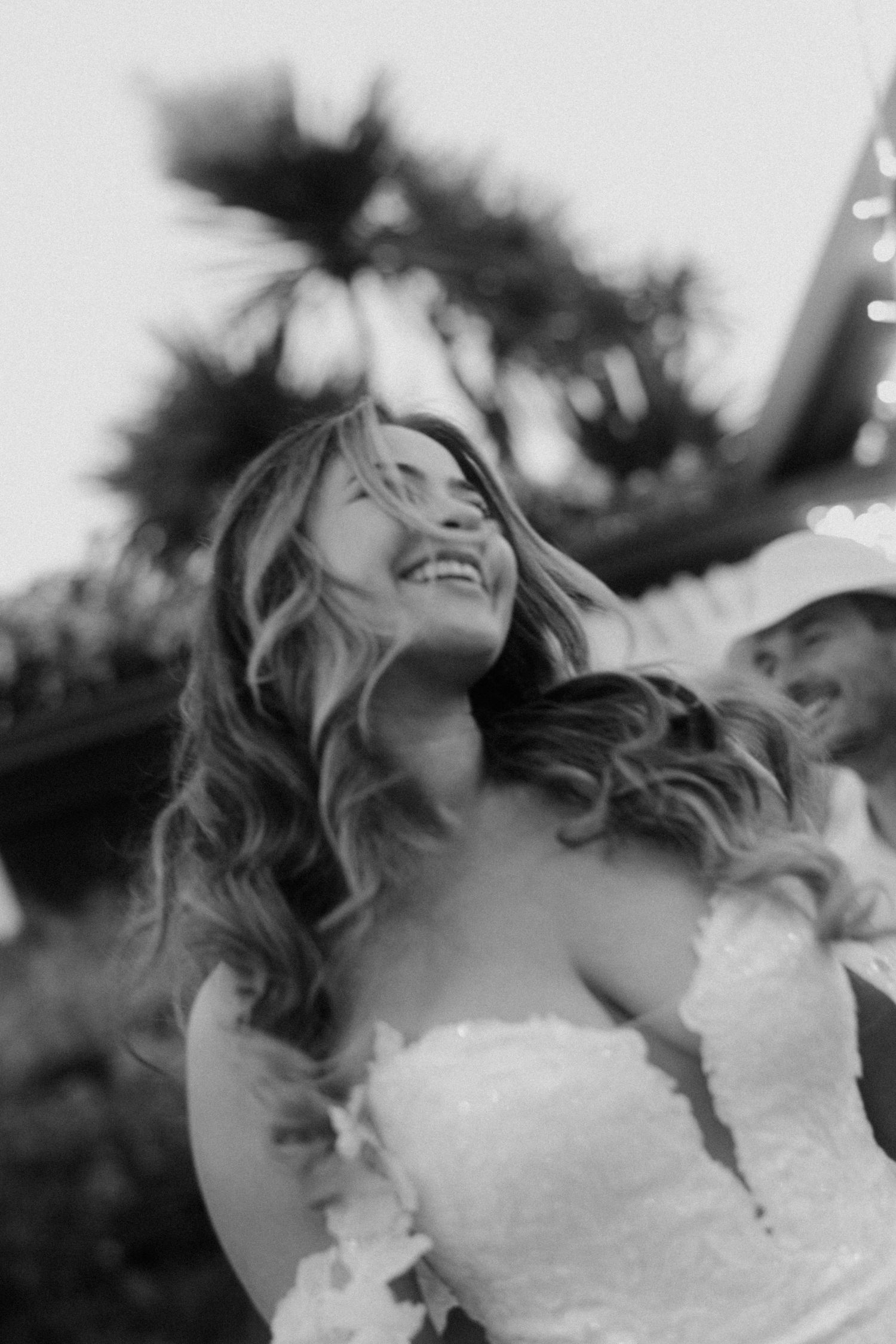 Black and white portrait of a joyful bride in a strapless wedding dress laughing with her hair flowing in the wind.