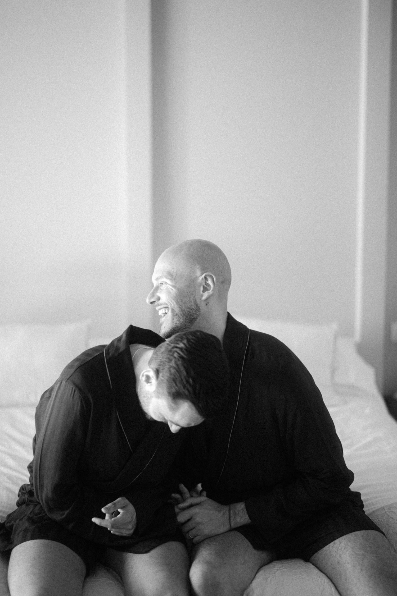 Black and white intimate portrait of two people sharing a tender moment while sitting together on a bed.