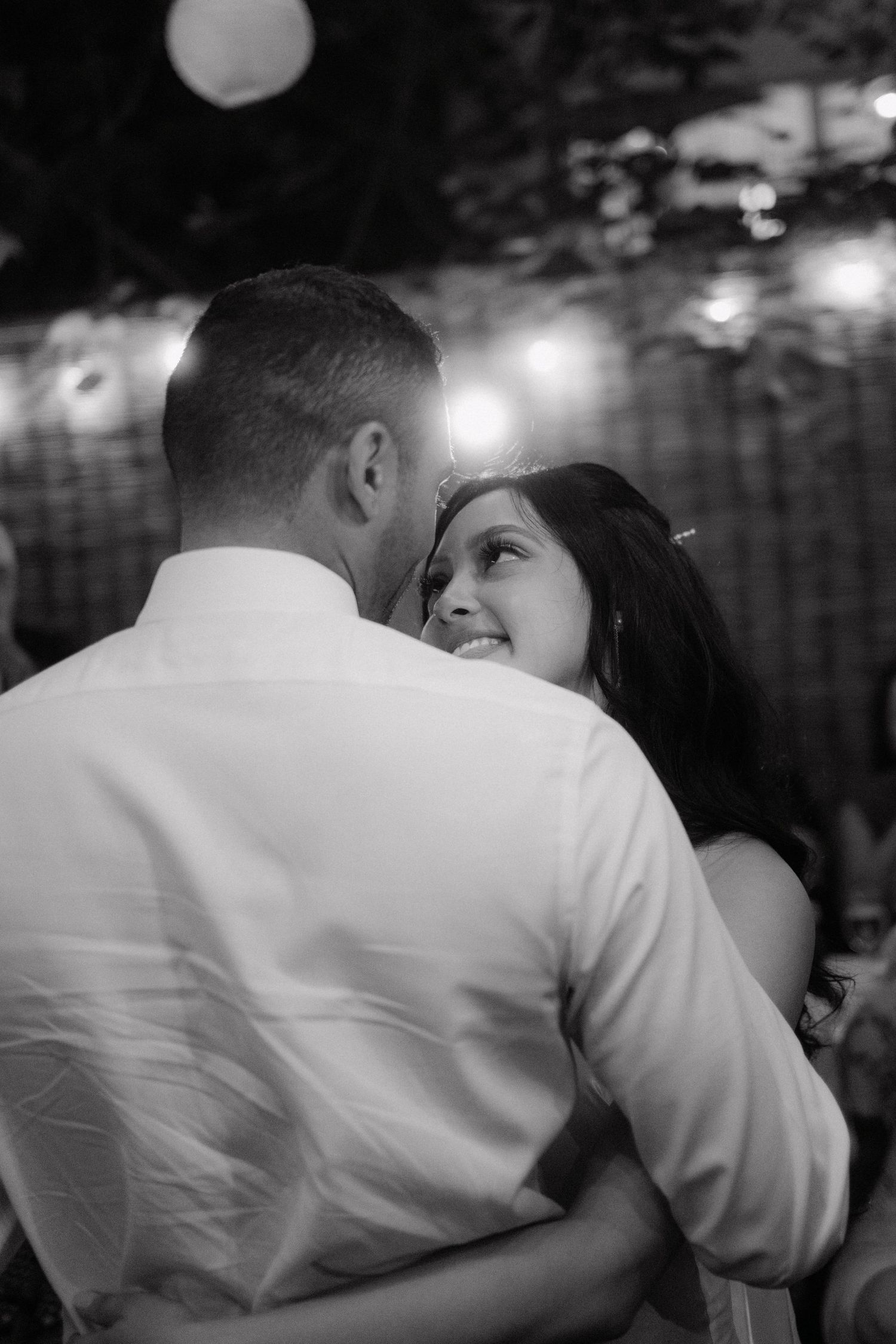 A romantic black and white moment captured during an evening dance with soft lights glowing in the background.