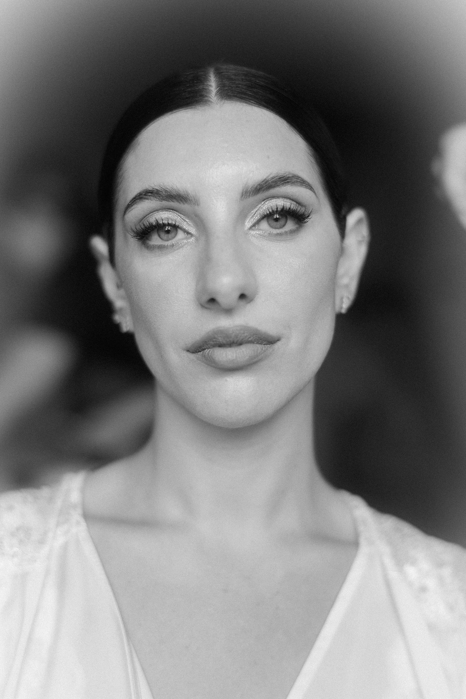 Black and white portrait of a young woman with dark hair, elegant makeup, and a white dress, gazing directly at camera.