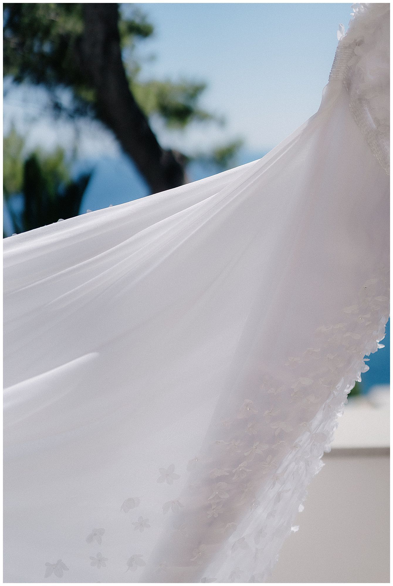 Close-up detail shot of flowing white wedding dress fabric against a bright blue sky background.