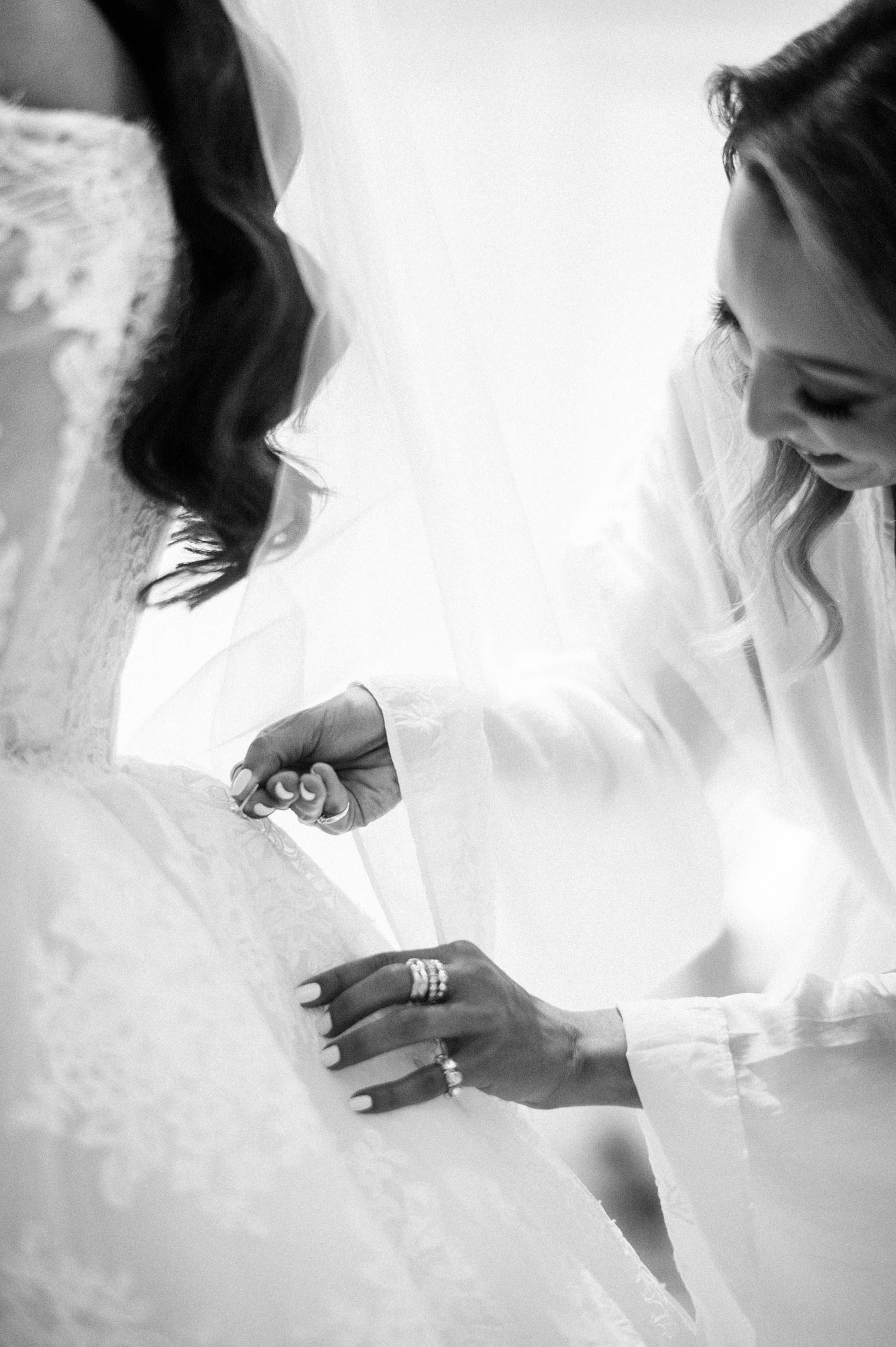 Black and white photo showing hands adjusting a wedding dress in an intimate getting ready moment.