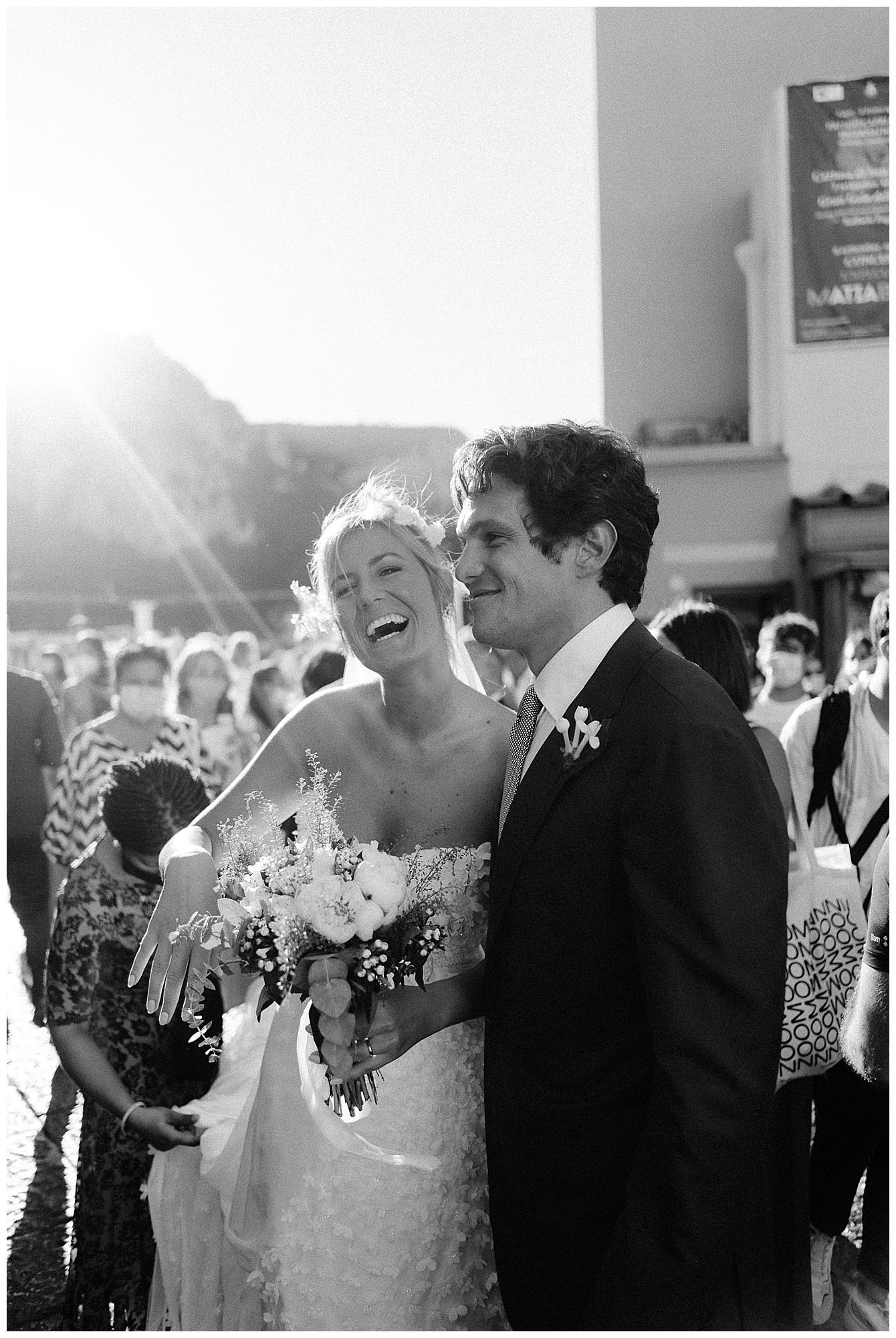 Black and white candid moment of a joyful newlywed couple laughing together during their outdoor wedding ceremony.