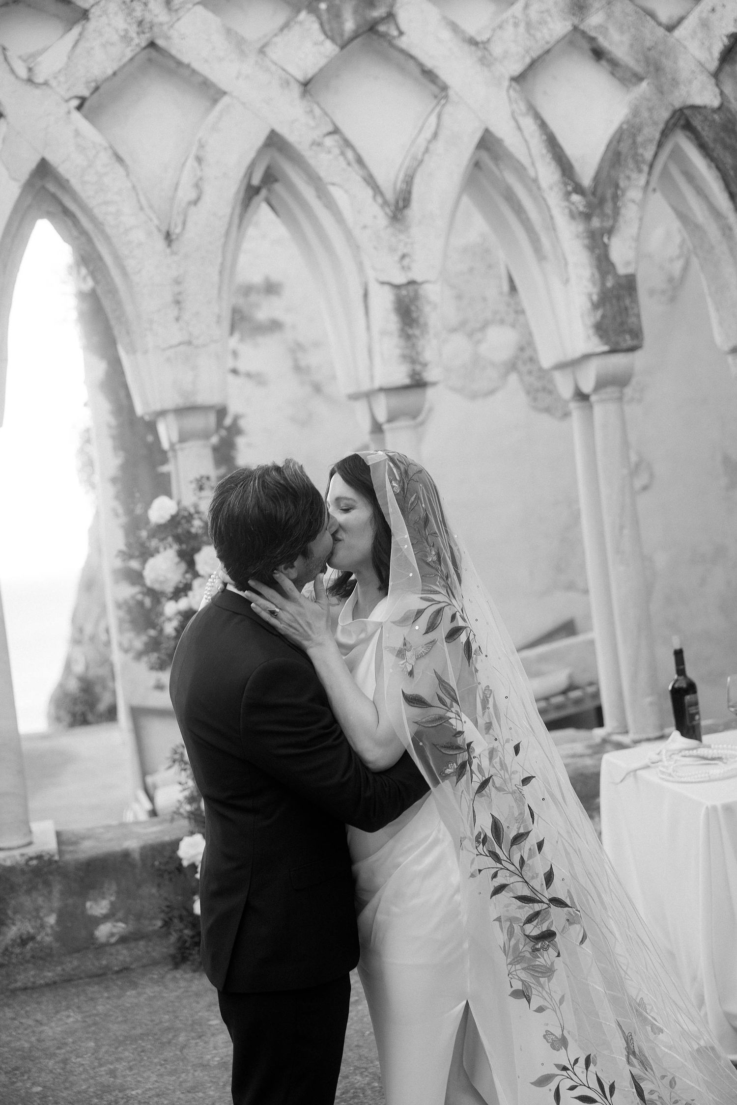 Black and white wedding photo sequence showing a romantic kiss under elegant stone archways at an outdoor venue.