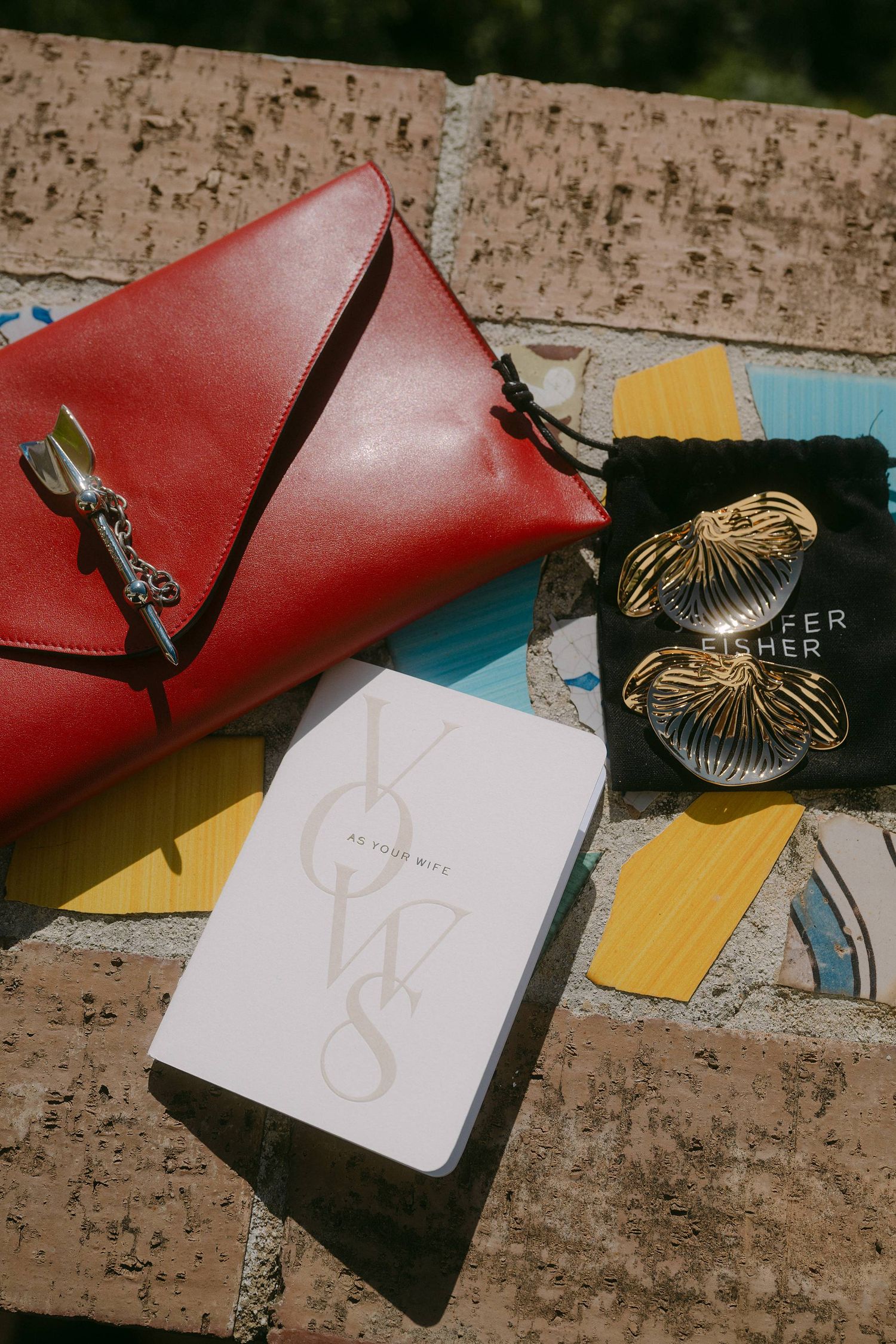 A red leather handbag displayed alongside a white notebook and gold butterfly-shaped jewelry in a green velvet pouch.