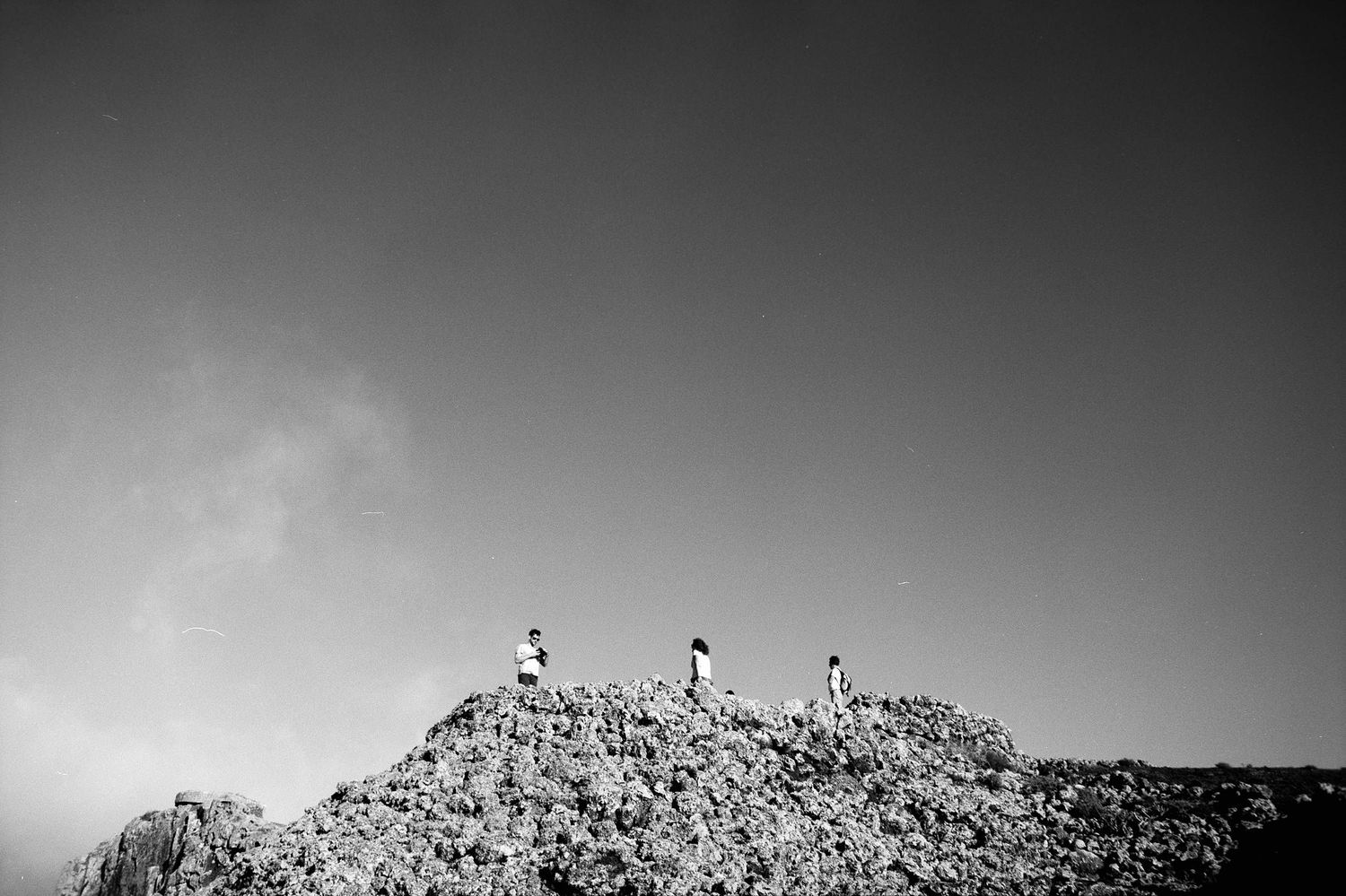 Several silhouetted figures stand atop a rocky ridge against a dramatic black and white sky.