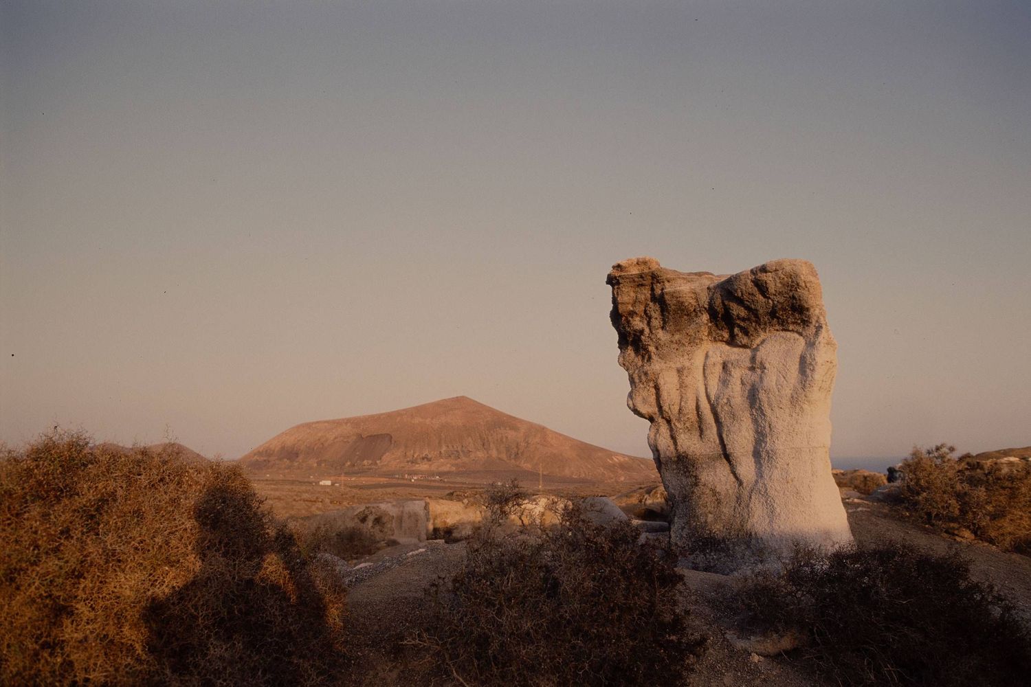 A weathered rock formation stands prominently against desert hills during golden hour sunset.