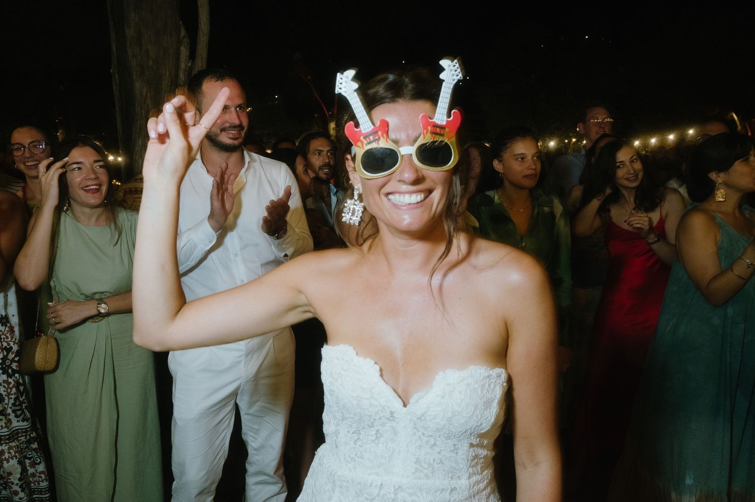 Bride wearing heart-shaped sunglasses dances joyfully at wedding reception celebration.