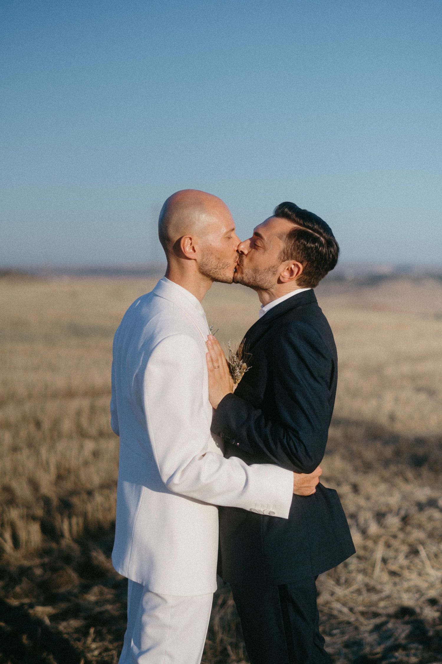 Two people share an intimate kiss against a desert landscape backdrop in a sequence of romantic photographs.