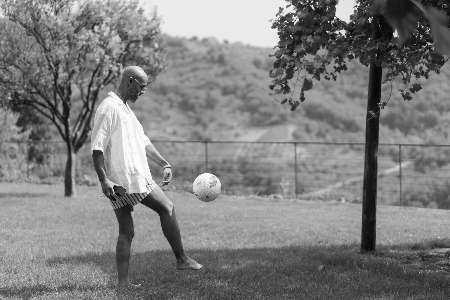 A person practices soccer skills in a backyard, juggling a ball in black and white vintage photograph.
