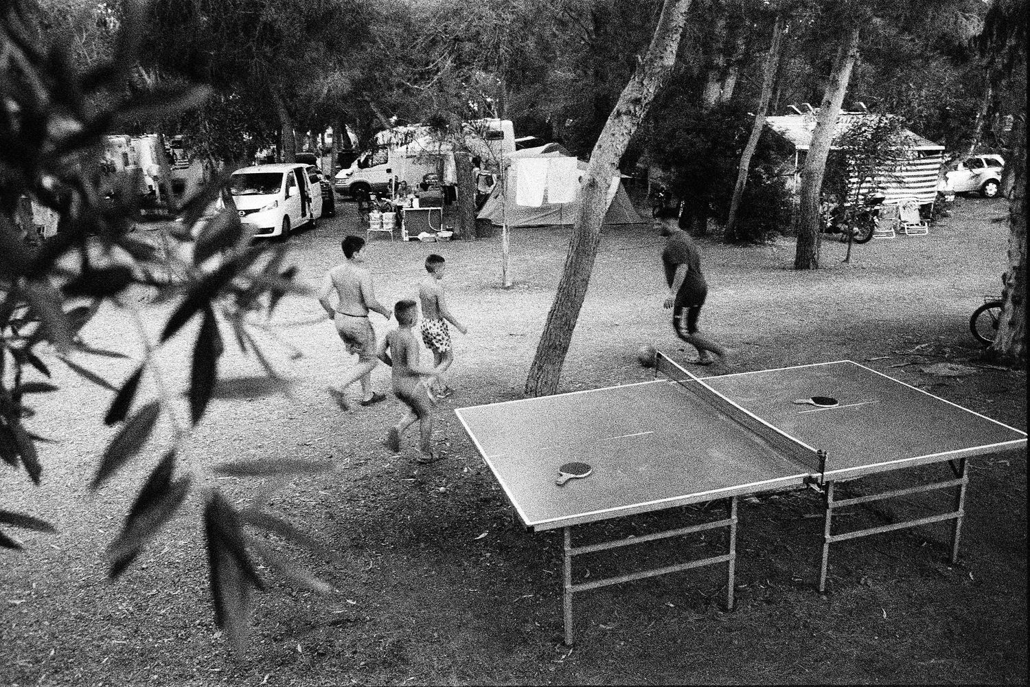 Vintage black and white photo showing people playing ping pong outdoors at a recreational gathering.