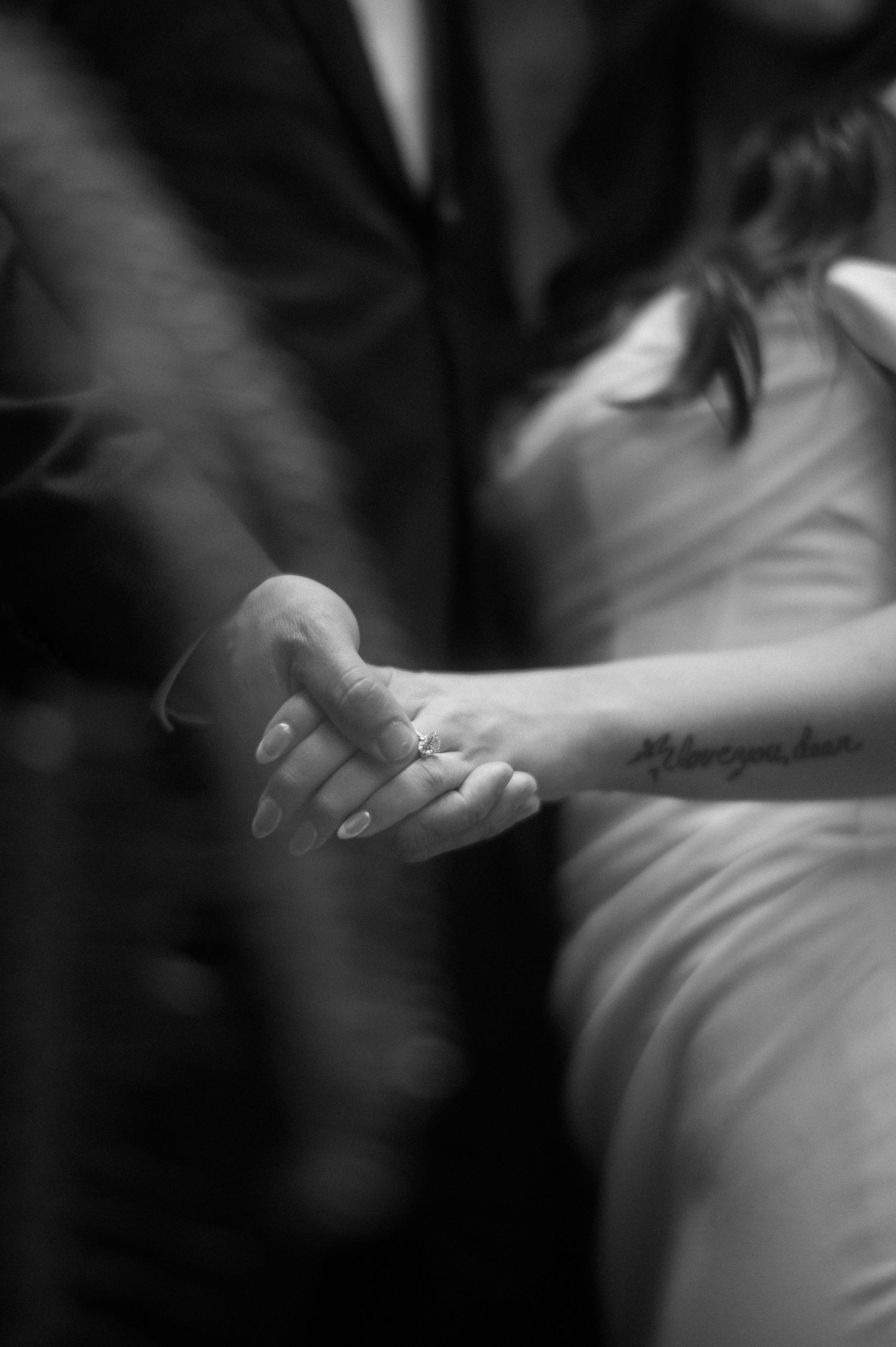 A black and white close-up photograph of two hands tenderly clasped together during a wedding ceremony.