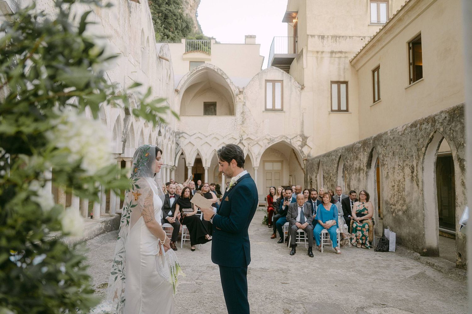 Wedding ceremony guests gather in a charming stone courtyard surrounded by historic architecture.