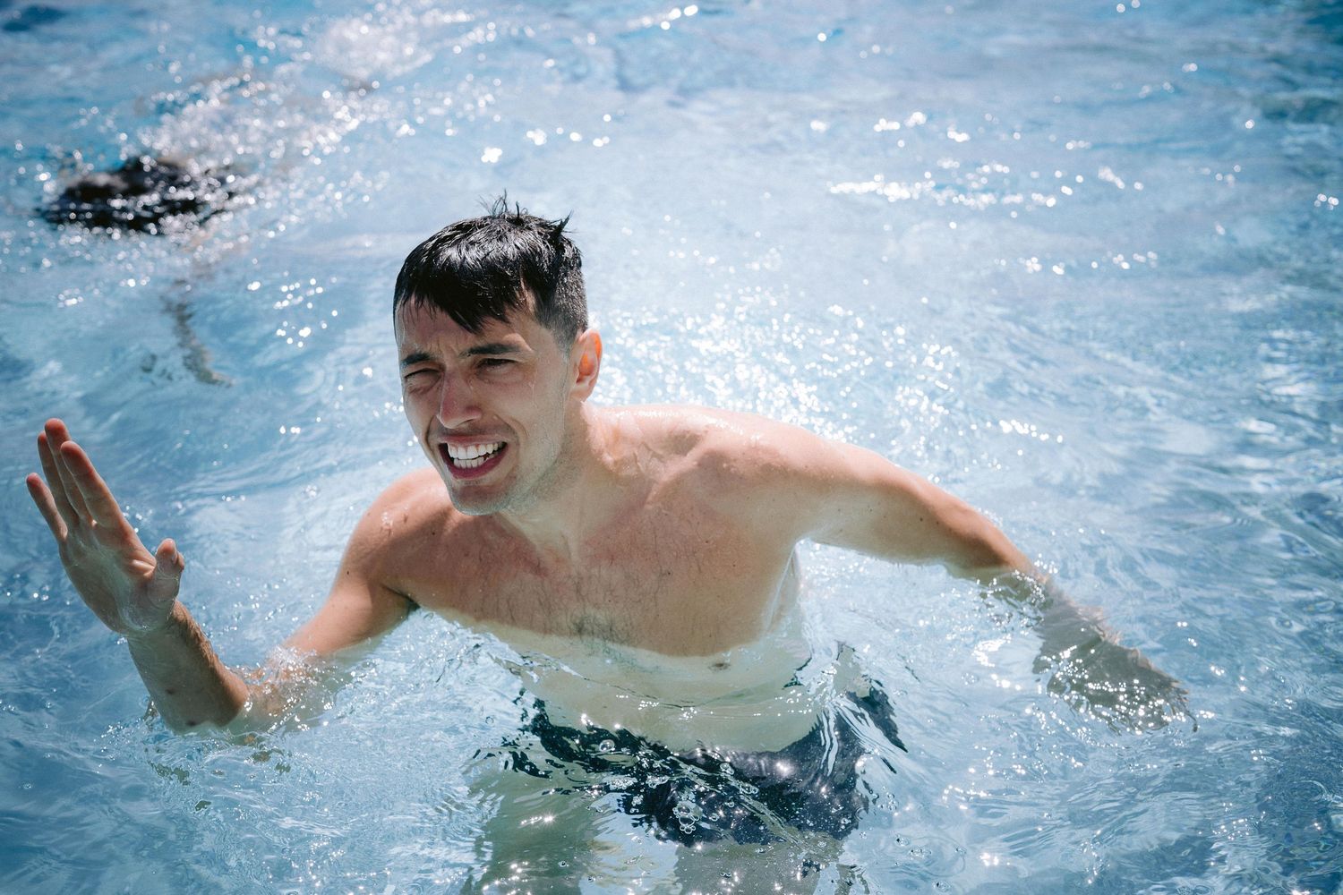 A sequence showing someone splashing and swimming freestyle in bright blue water sparkling with sunlight from above.