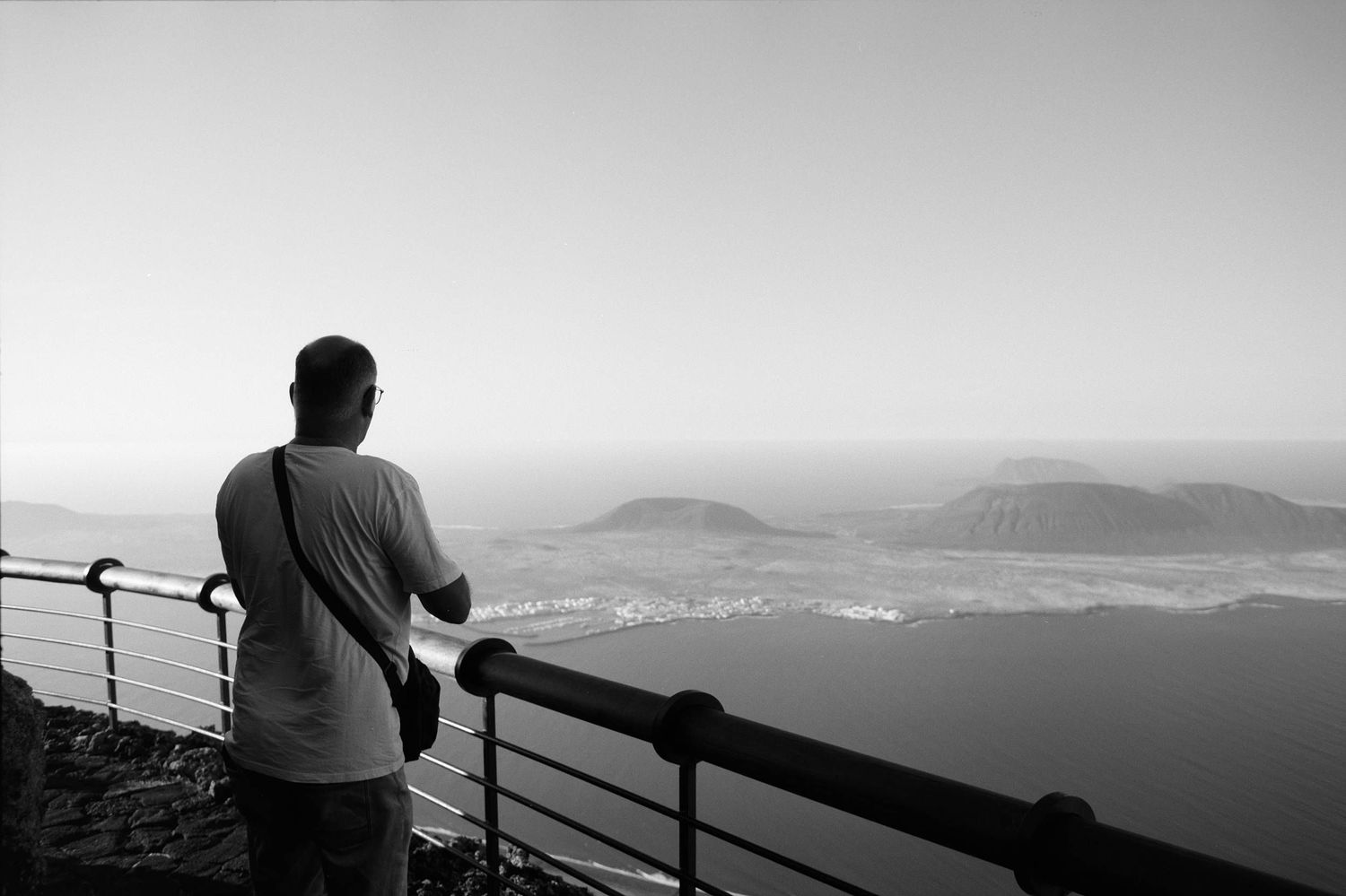 A lone person looks out over a misty mountain landscape while standing at a railing on a scenic overlook.