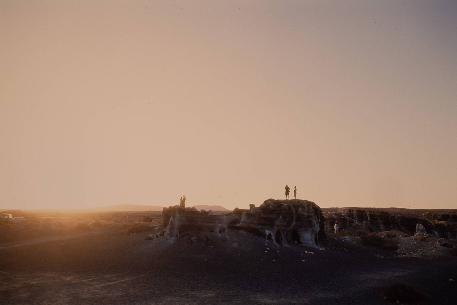 Two silhouetted figures stand on a hilltop against a warm sunset sky creating a dramatic outdoor landscape.