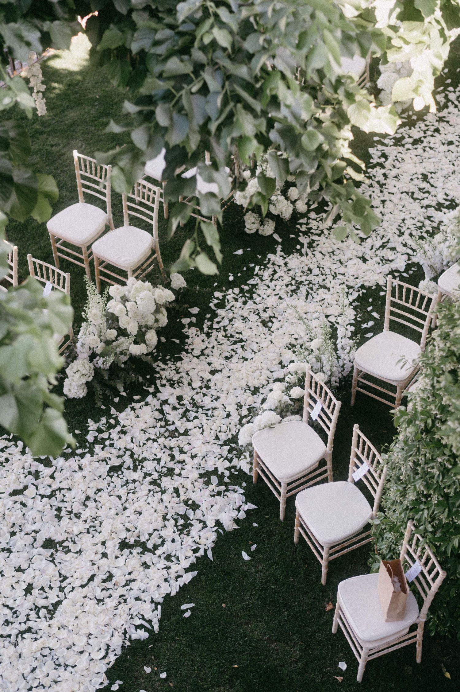 White chiavari chairs line a petal-strewn aisle at an elegant outdoor garden wedding ceremony setup.