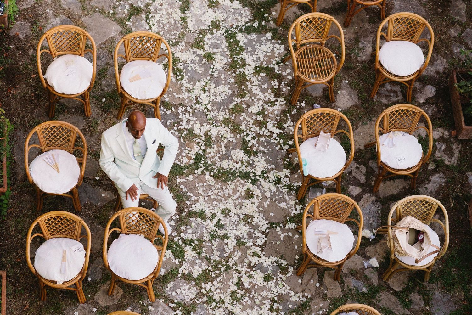 A series of white paper lanterns and woven rattan chairs arranged in a rustic outdoor setting against a stone wall.