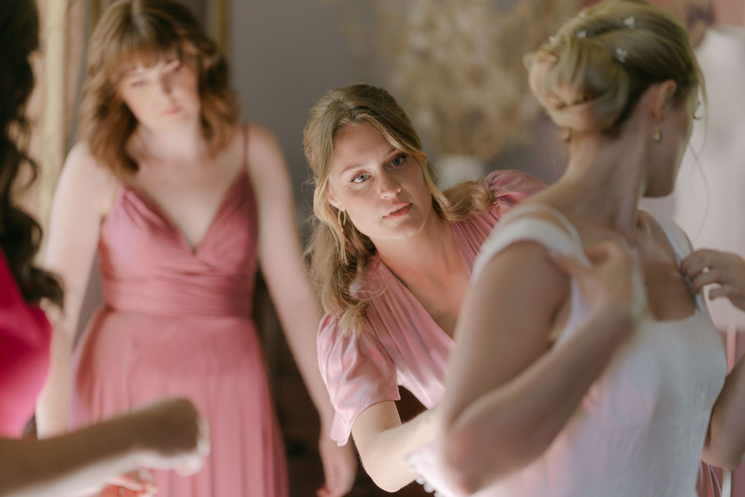 A group of bridesmaids in pink dresses help the bride prepare for her wedding day.