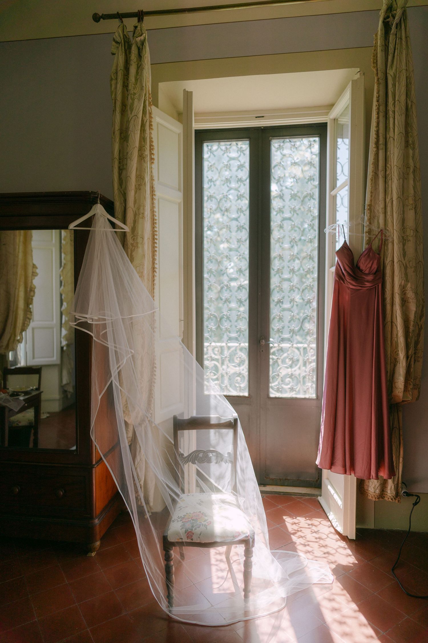 Sunlight streams through windows onto a white mosquito net canopy draped over a chair in a minimalist room.
