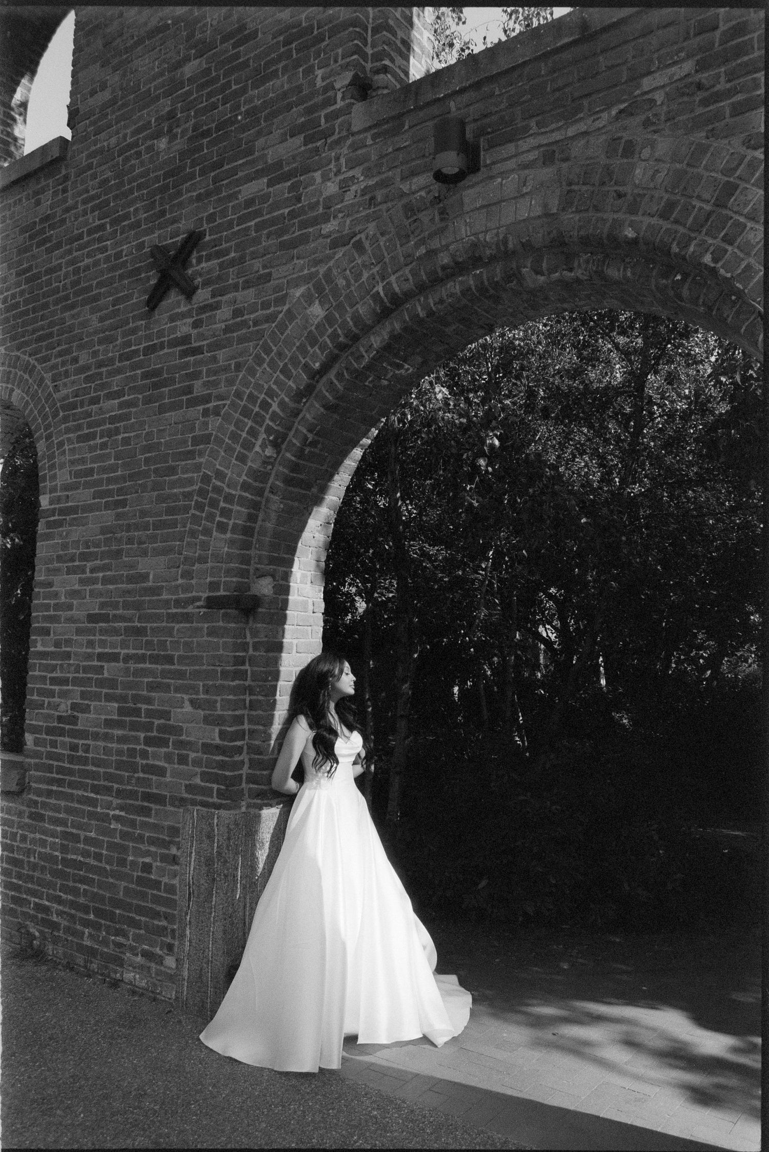 A bride in a flowing white wedding gown poses against a brick wall in a series of black and white photographs.