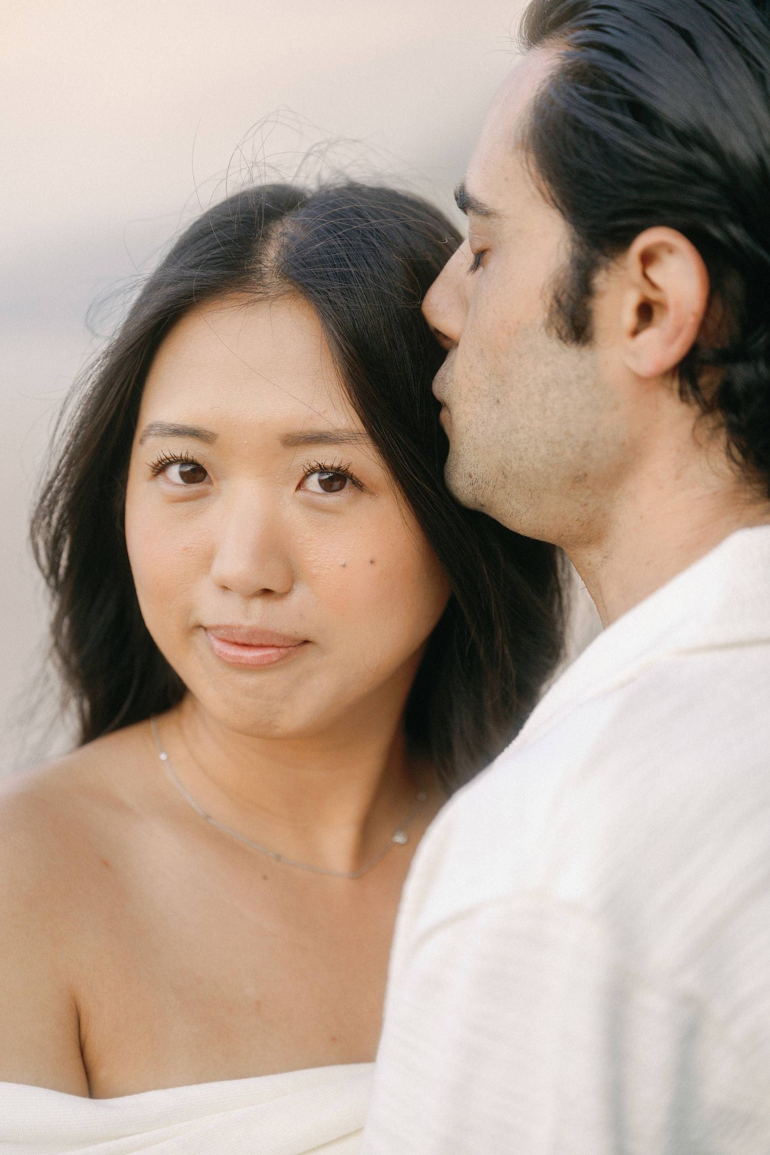 Romantic close up portrait of a couple in white attire against a soft pastel background.