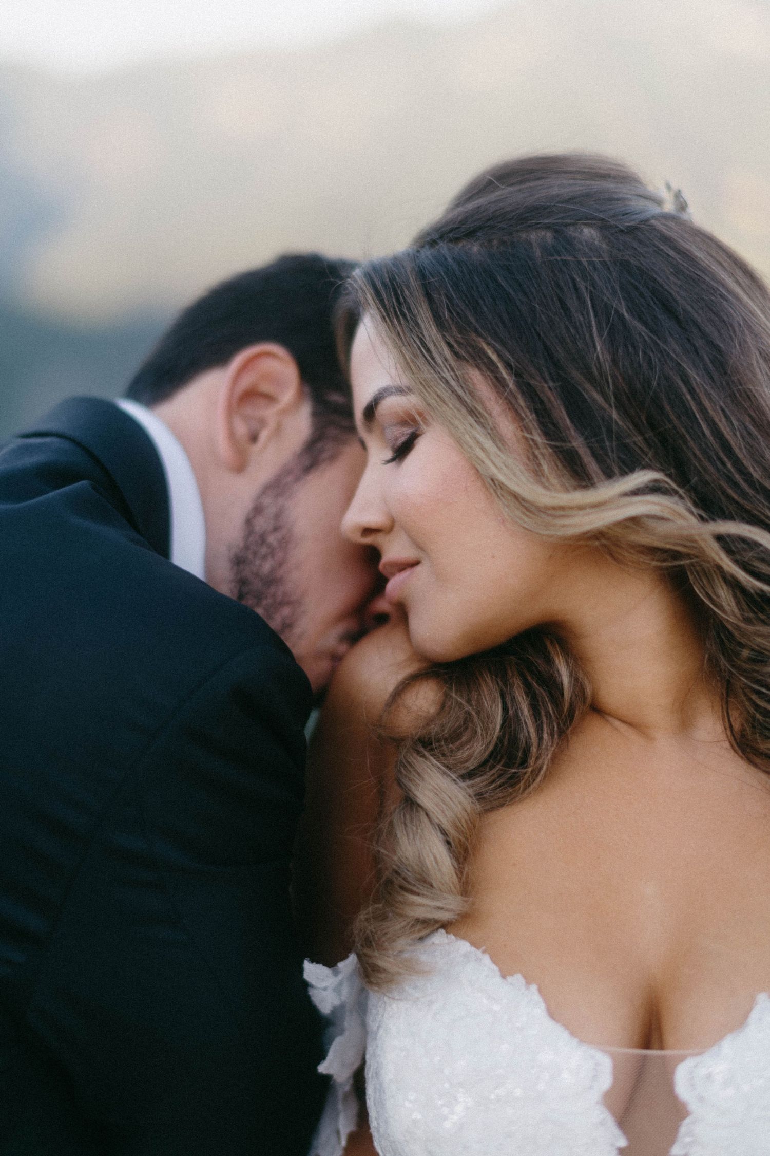 A romantic wedding portrait shows a couple in white dress and dark suit embracing in soft lighting.