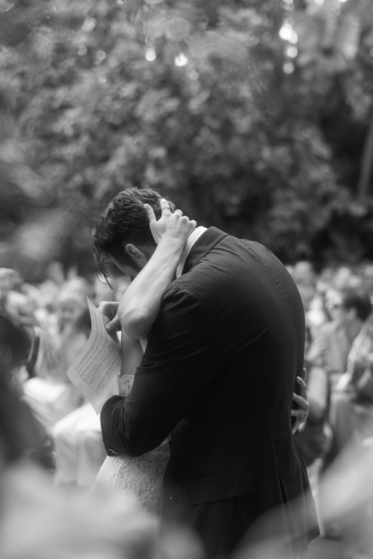 Black and white wedding photo showing an intimate embrace during an outdoor garden ceremony.