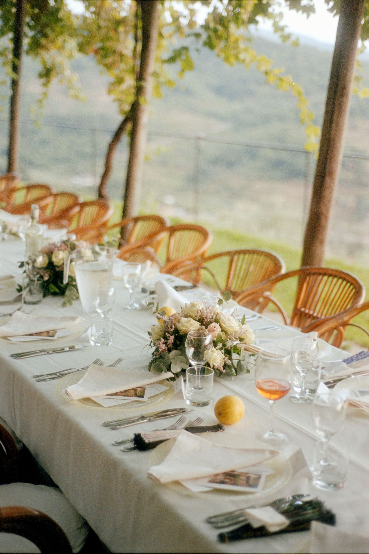 Elegant wedding reception tables set with white linens, floral centerpieces and rattan chairs overlooking a scenic view.