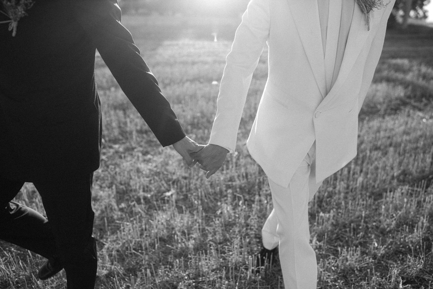 A romantic couple in formal wedding attire embraces in a sunlit outdoor garden setting.